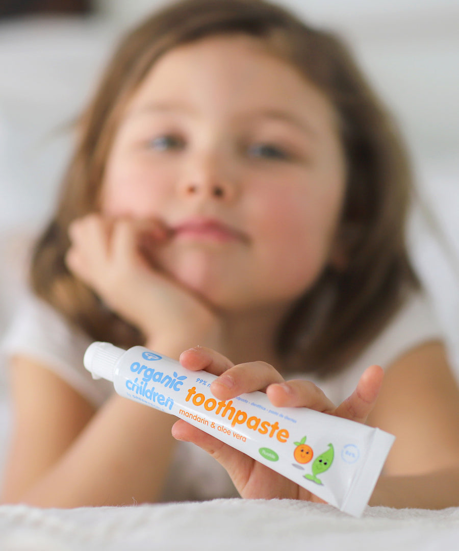 A child holding on a tube of Organic Children Toothpaste Mandarin & Aloe Vera with Fluoride. 