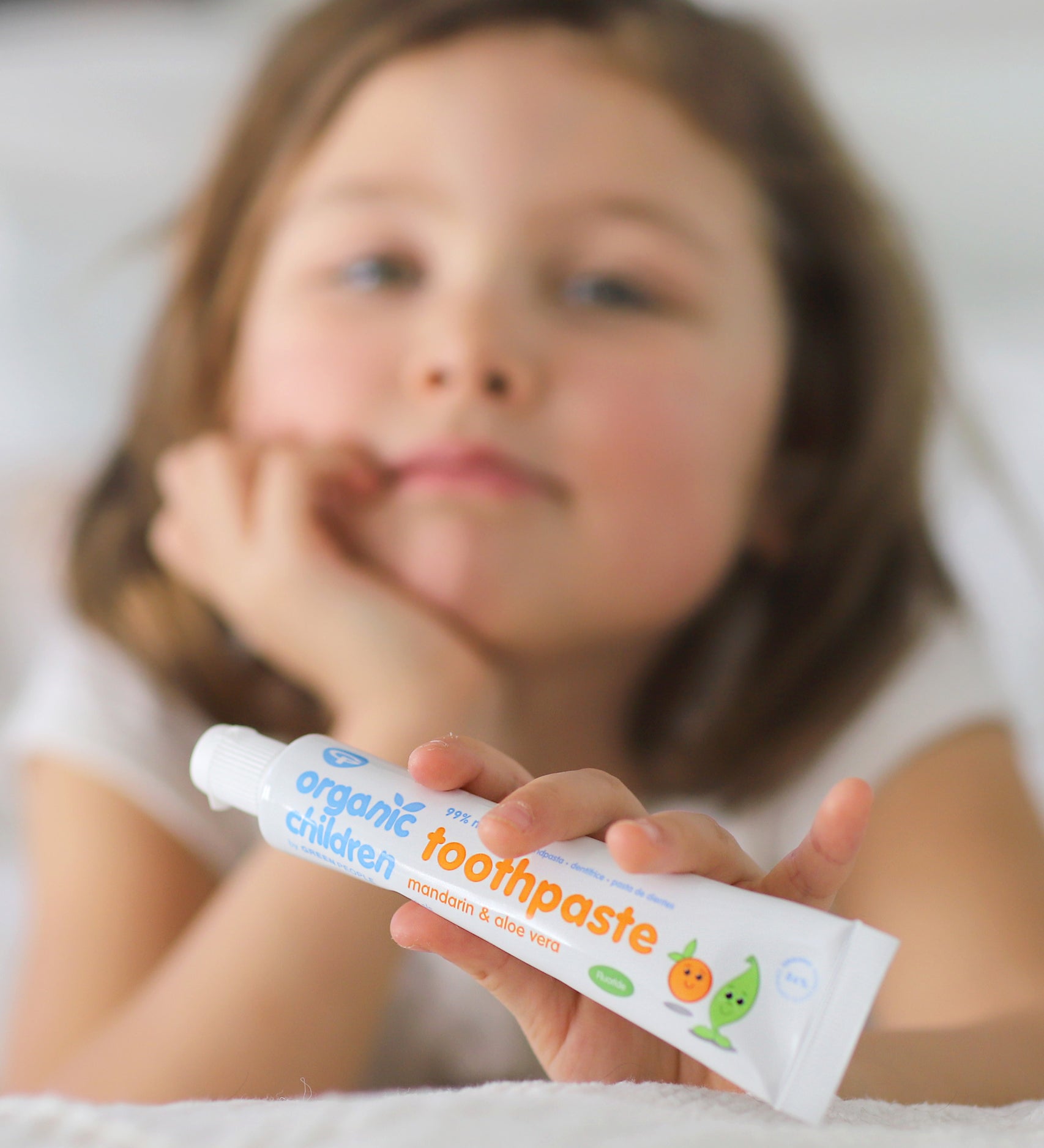 A child holding on a tube of Organic Children Toothpaste Mandarin & Aloe Vera with Fluoride. 