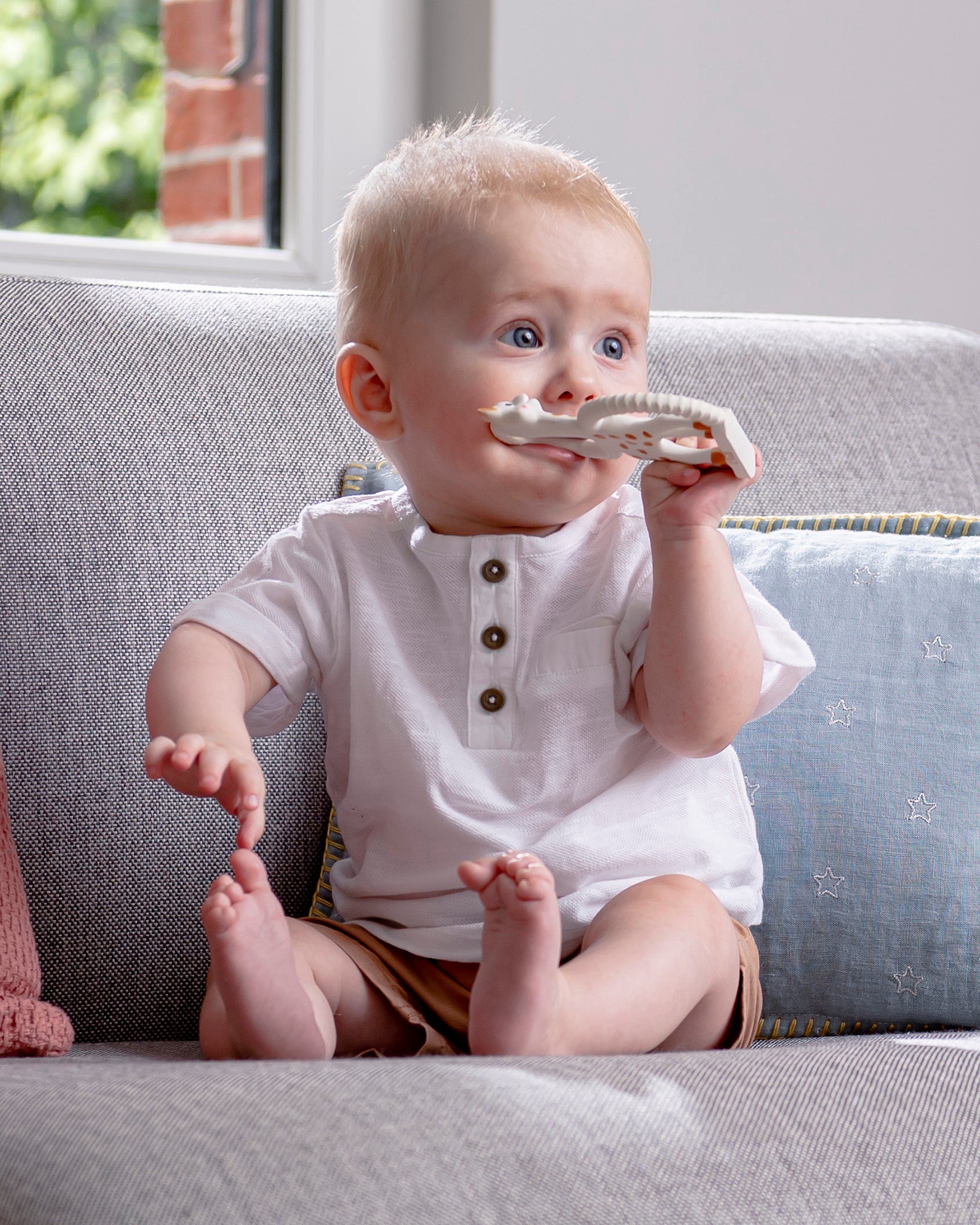 A child in a blue dress chewing on the Sophie The Giraffe So Pure Soft Teething Ring