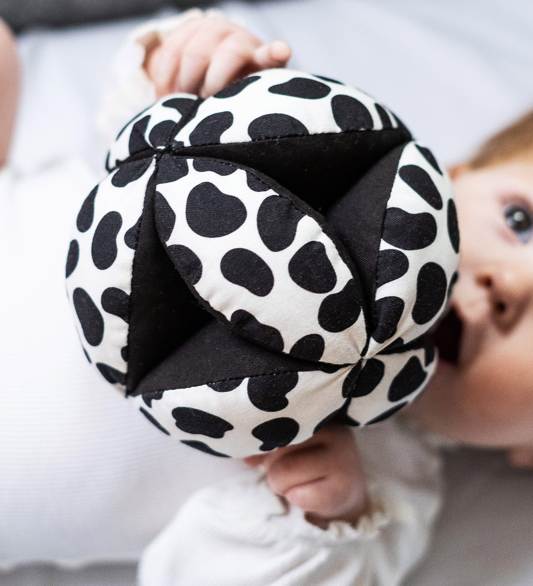 Etta Loves Organic Sensory Grasping Ball with black and white spots, and a black inner, being played with by a child