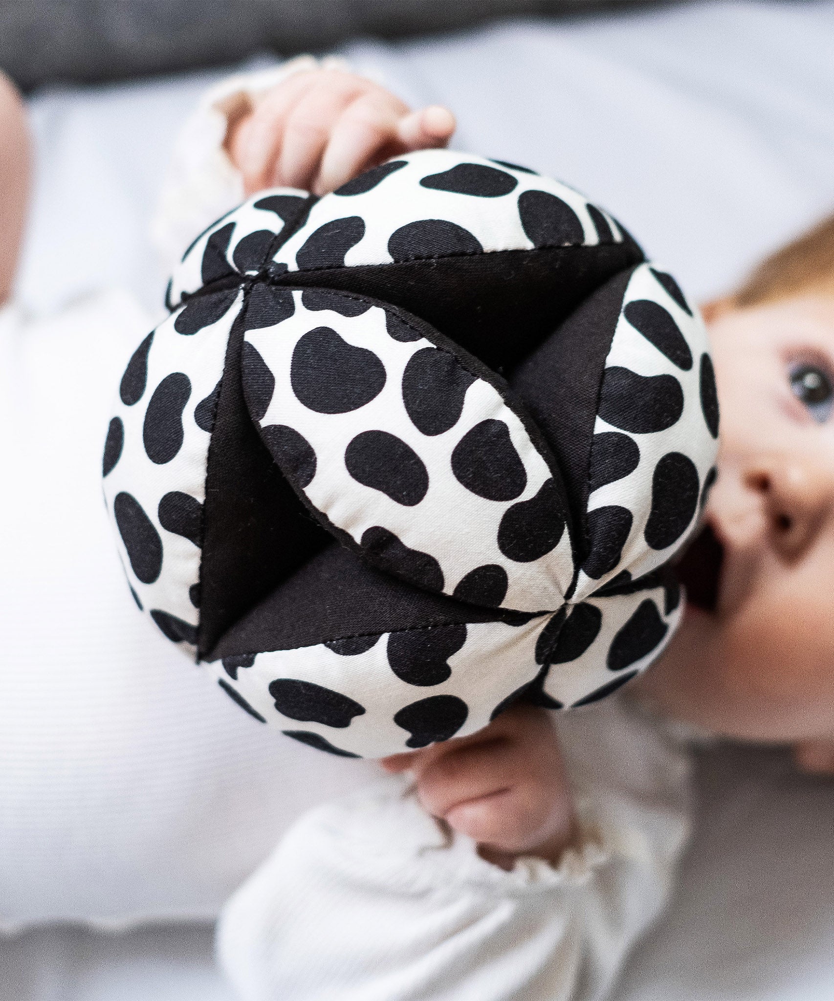 Etta Loves Organic Sensory Grasping Ball with black and white spots, and a black inner, being played with by a child