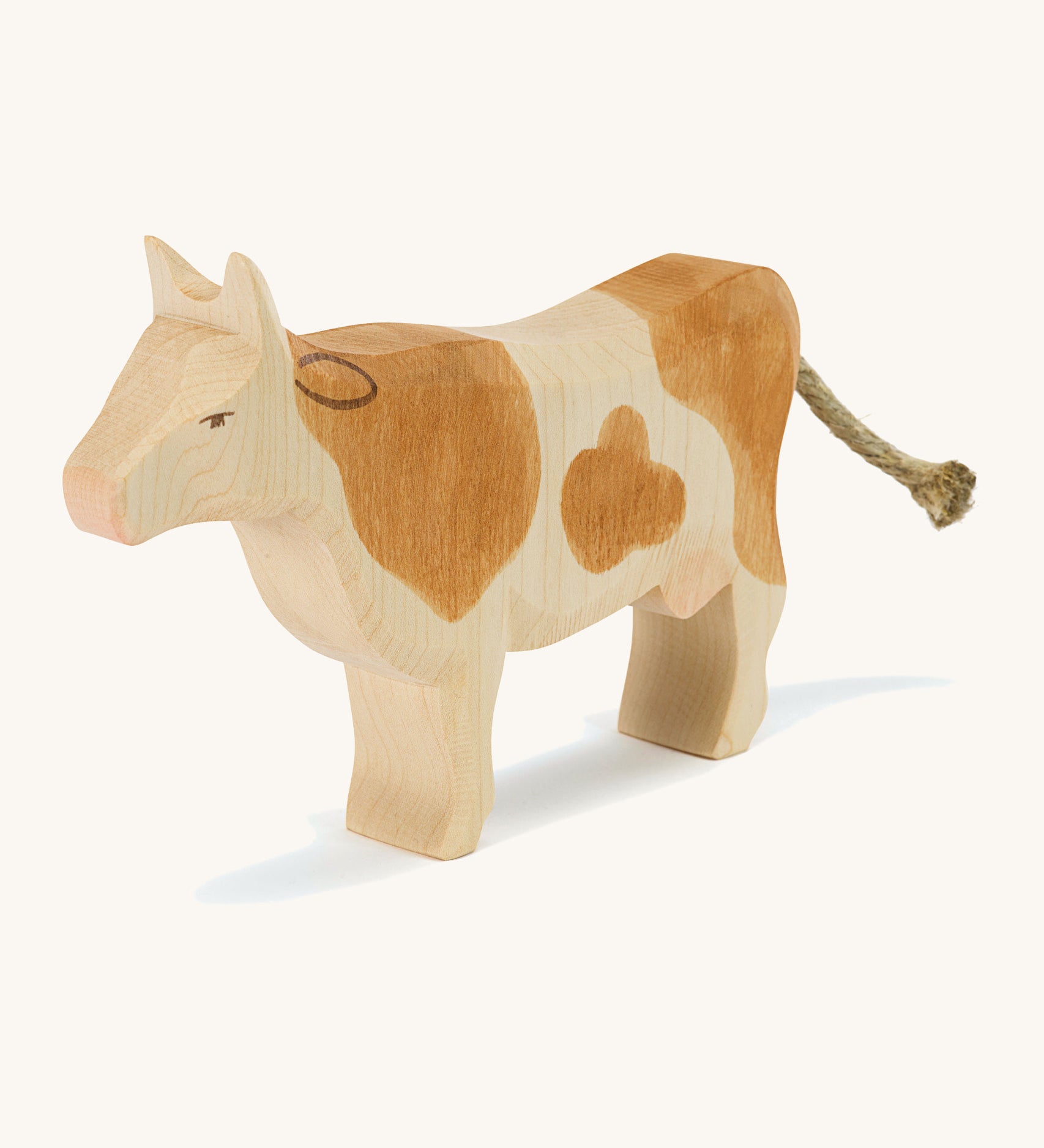 A brown wooden Ostheimer standing cow figure on a cream background.