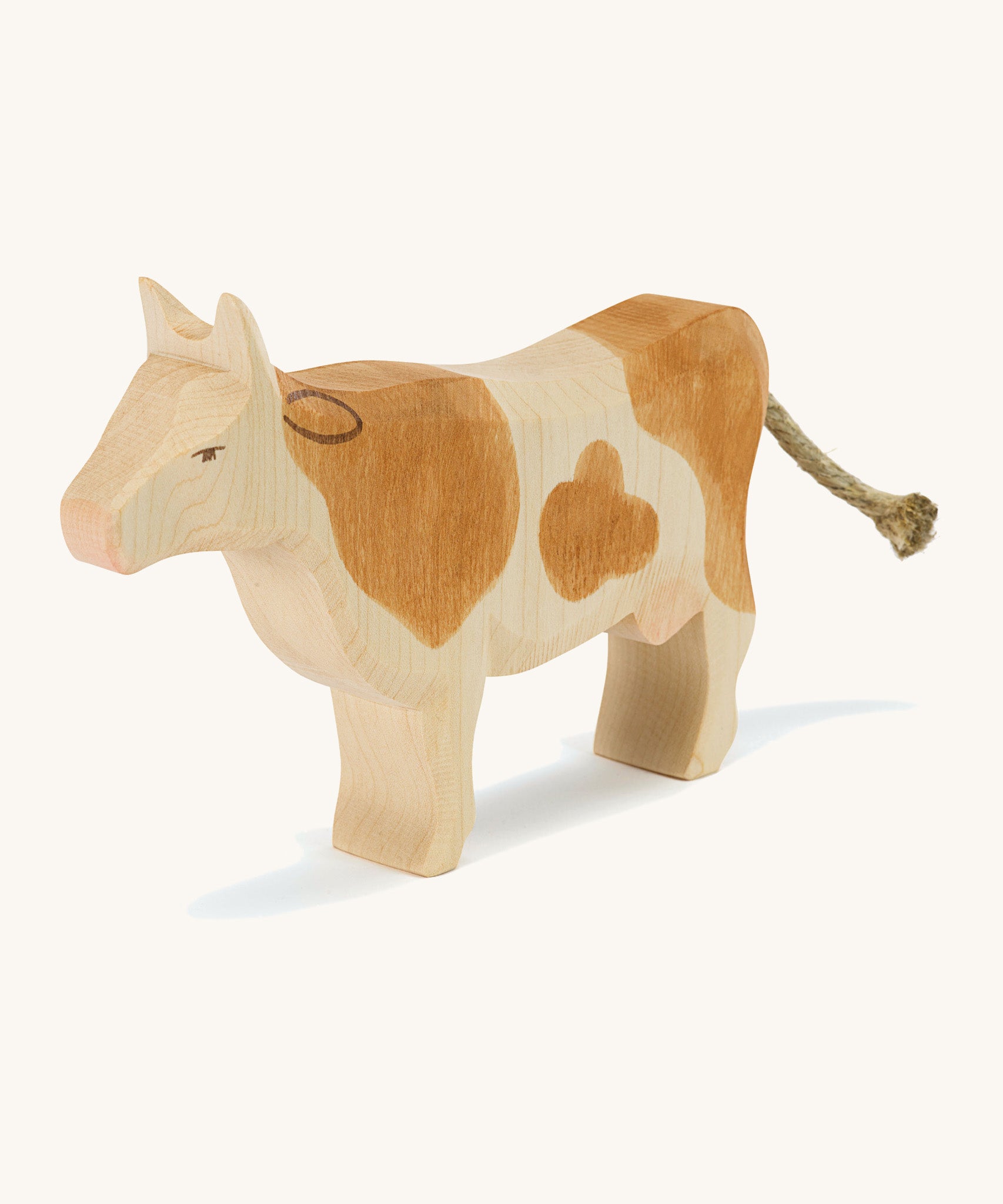 A brown wooden Ostheimer standing cow figure on a cream background.