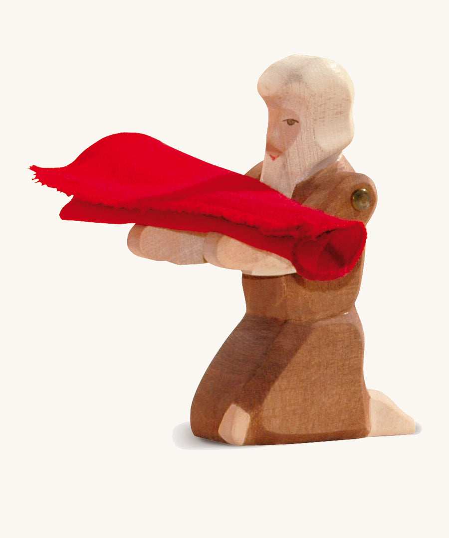 A kneeling wooden beggar figure holding a piece of red cloth on a cream background