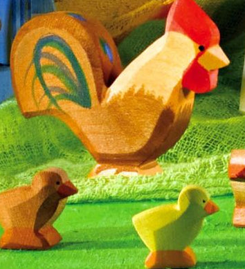 A brown Ostheimer rooster pictured in a small world play set up with small brown and yellow chicks on a green felt surface. 