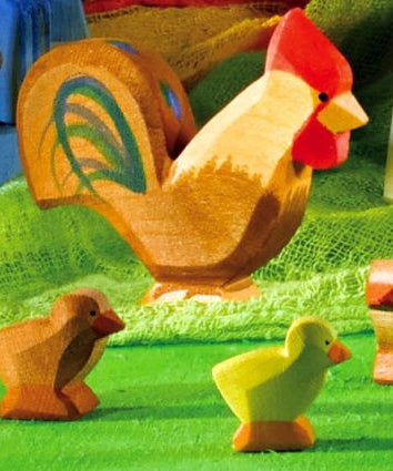 A brown Ostheimer rooster pictured in a small world play set up with small brown and yellow chicks on a green felt surface. 