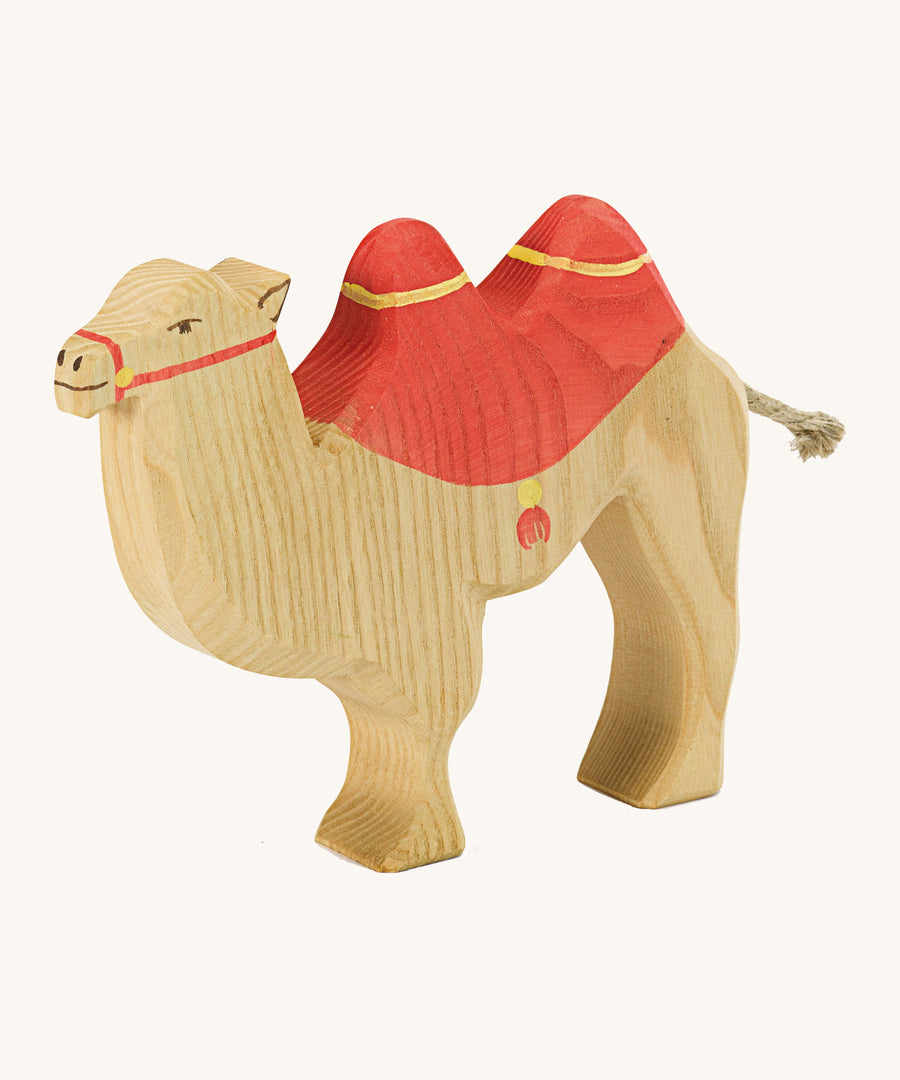 A brown wooden camel figure with a red saddle on a cream background