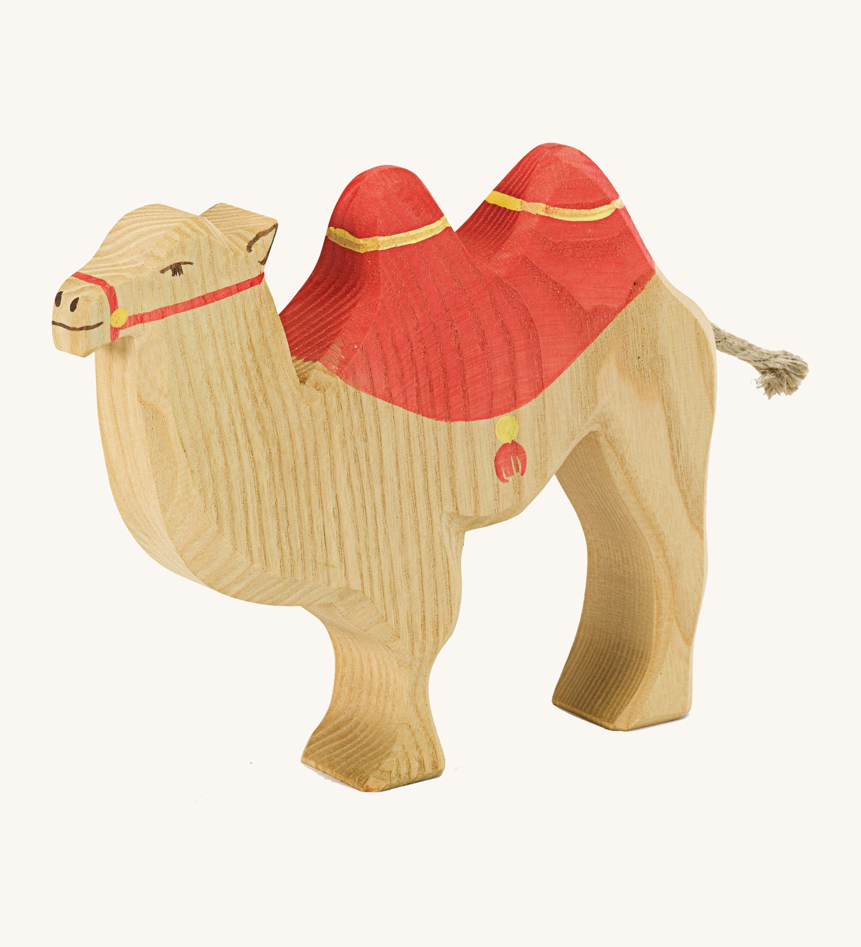 A brown wooden camel figure with a red saddle on a cream background