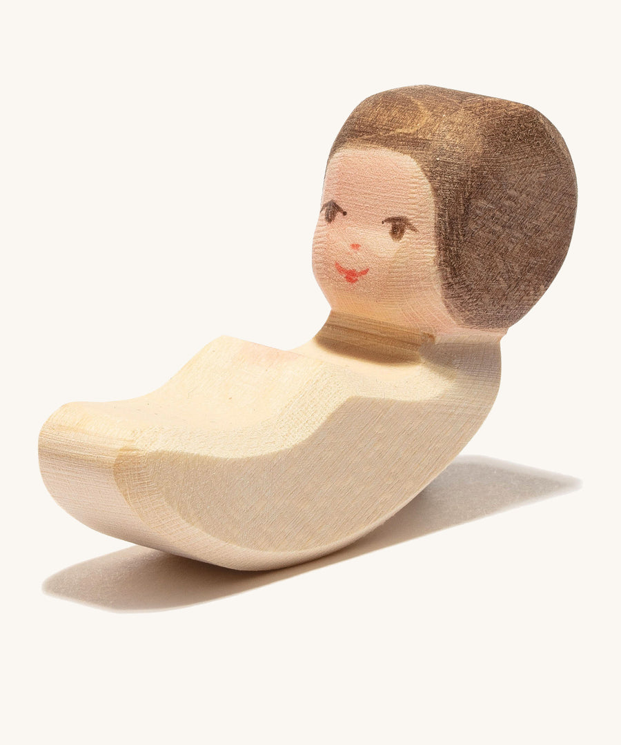 A wooden lying child figure that's compatible with the cradle on a cream background.