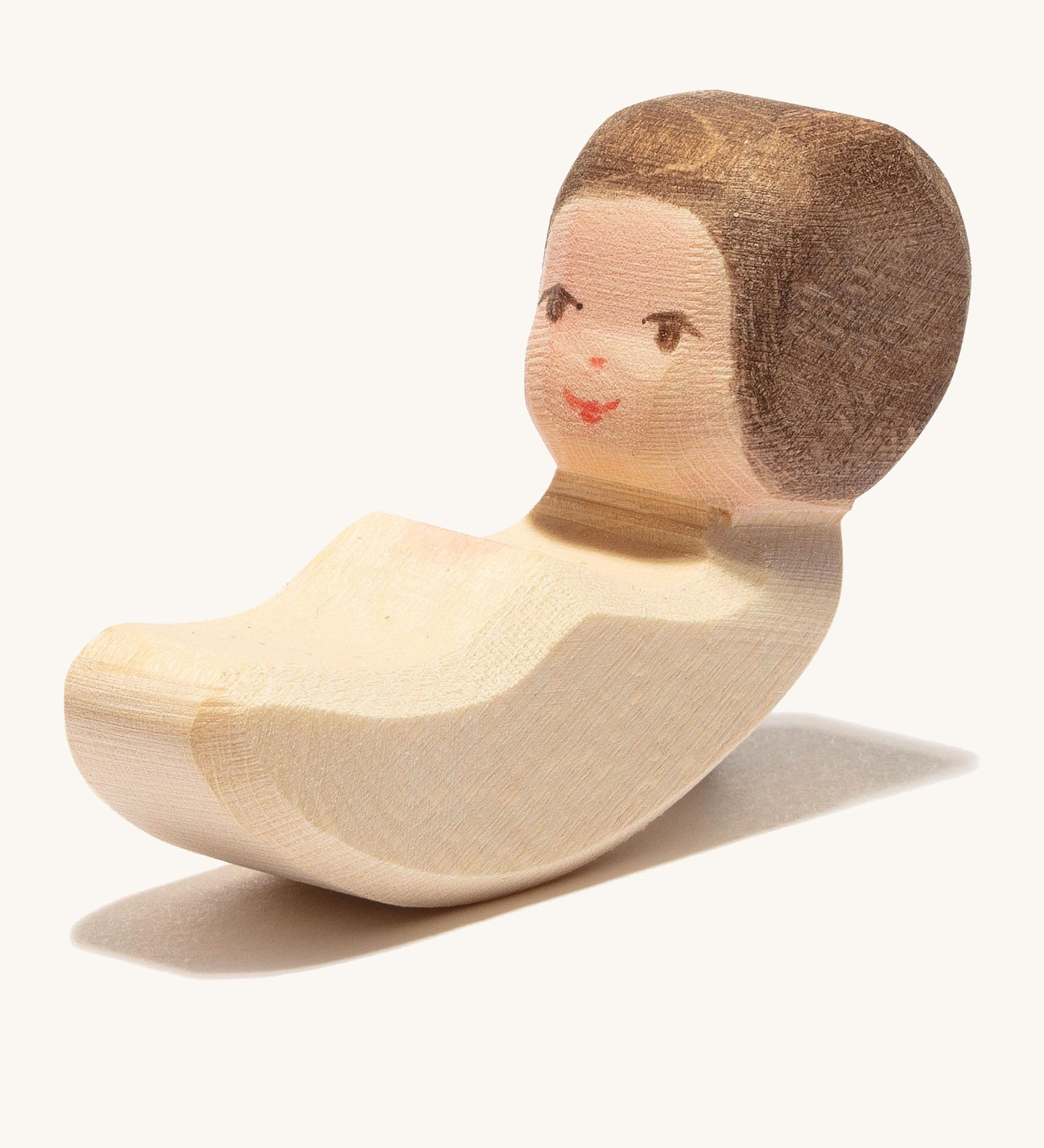 A wooden lying child figure that's compatible with the cradle on a cream background.