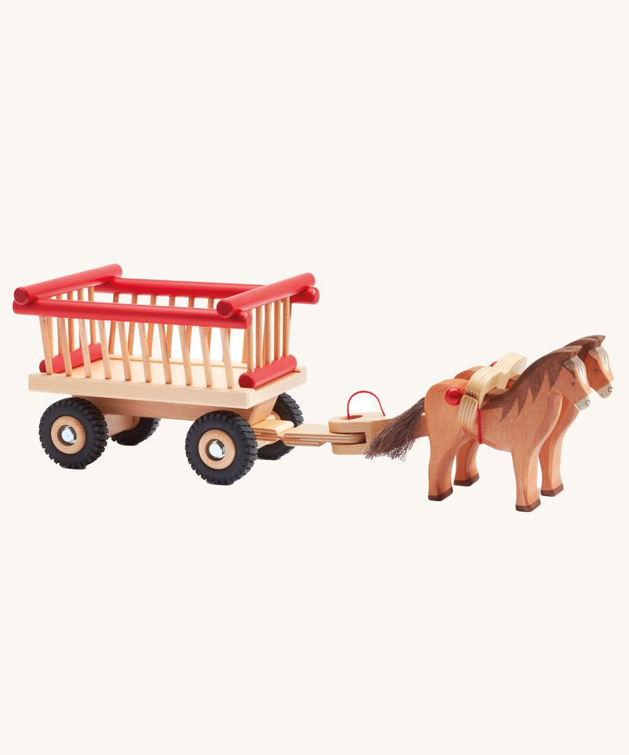 Ostheimer wooden hay-cart with red details on a plain background. The cart is attached to two horses with the horse harness.  