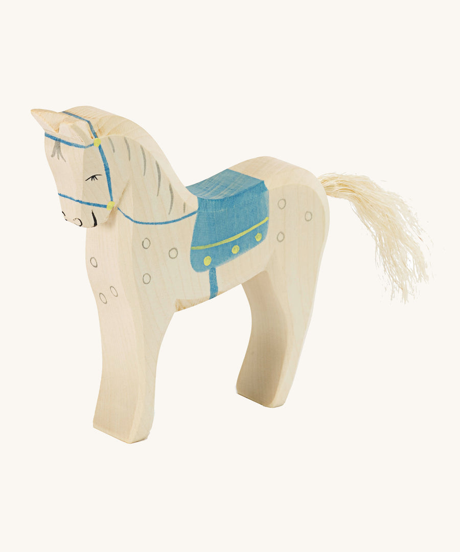 A white wooden horse figure with a blue saddle on a cream background