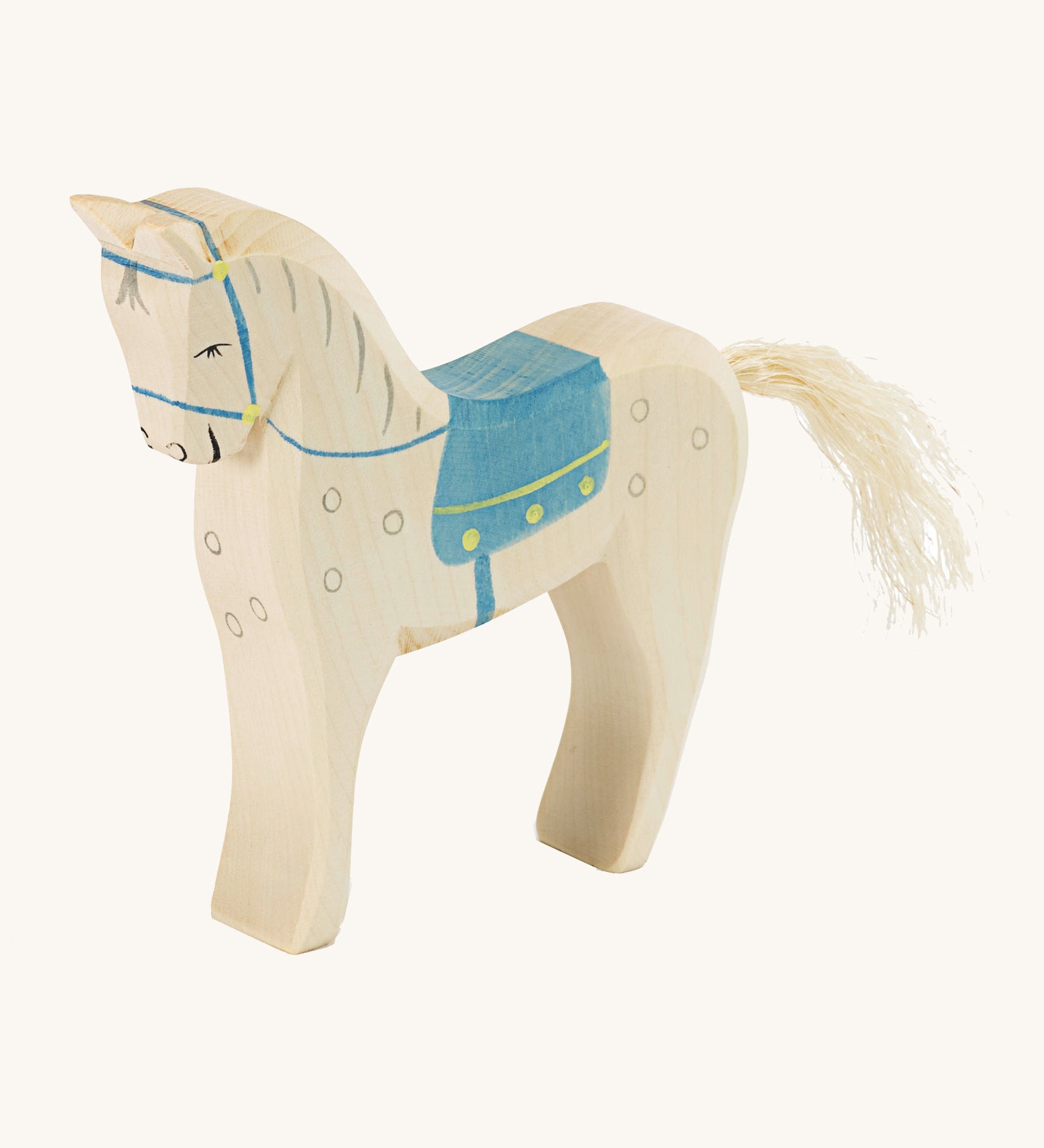 A white wooden horse figure with a blue saddle on a cream background