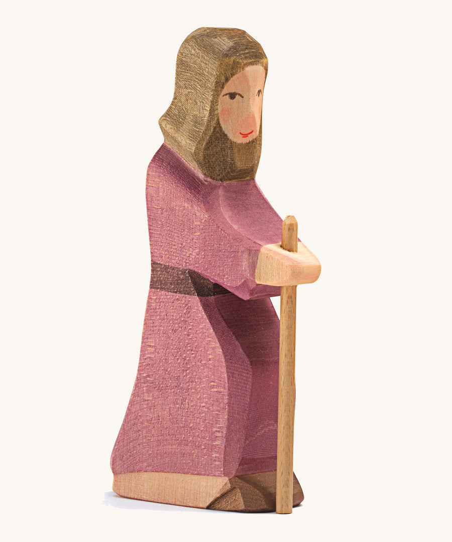 A Joseph wooden figure wearing a purple robe holding a wooden staff on a cream background