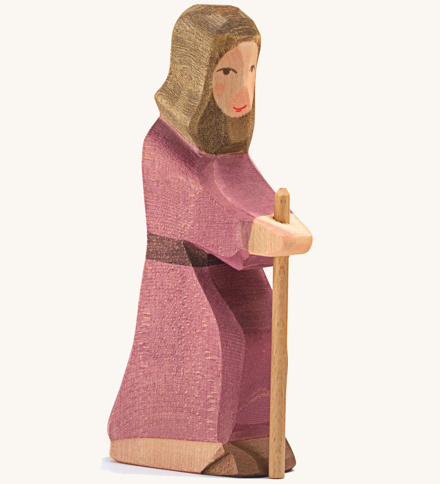 A Joseph wooden figure wearing a purple robe holding a wooden staff on a cream background