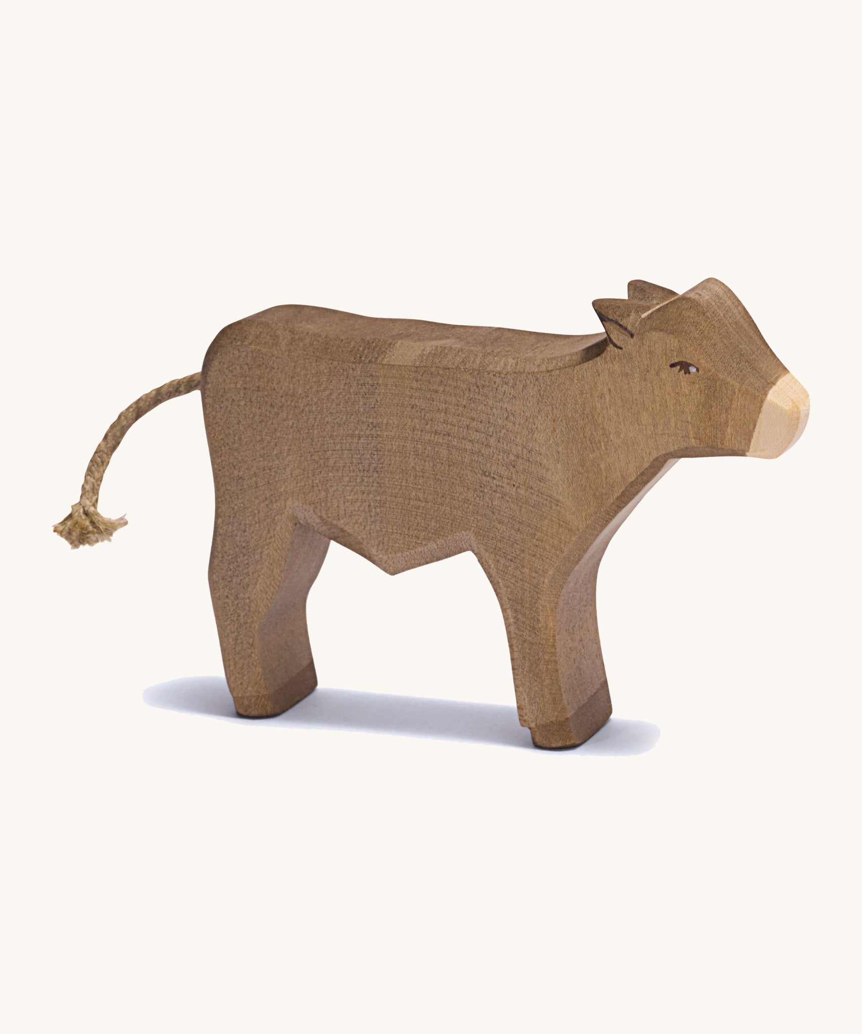 A brown standing wooden ox figure on a cream background