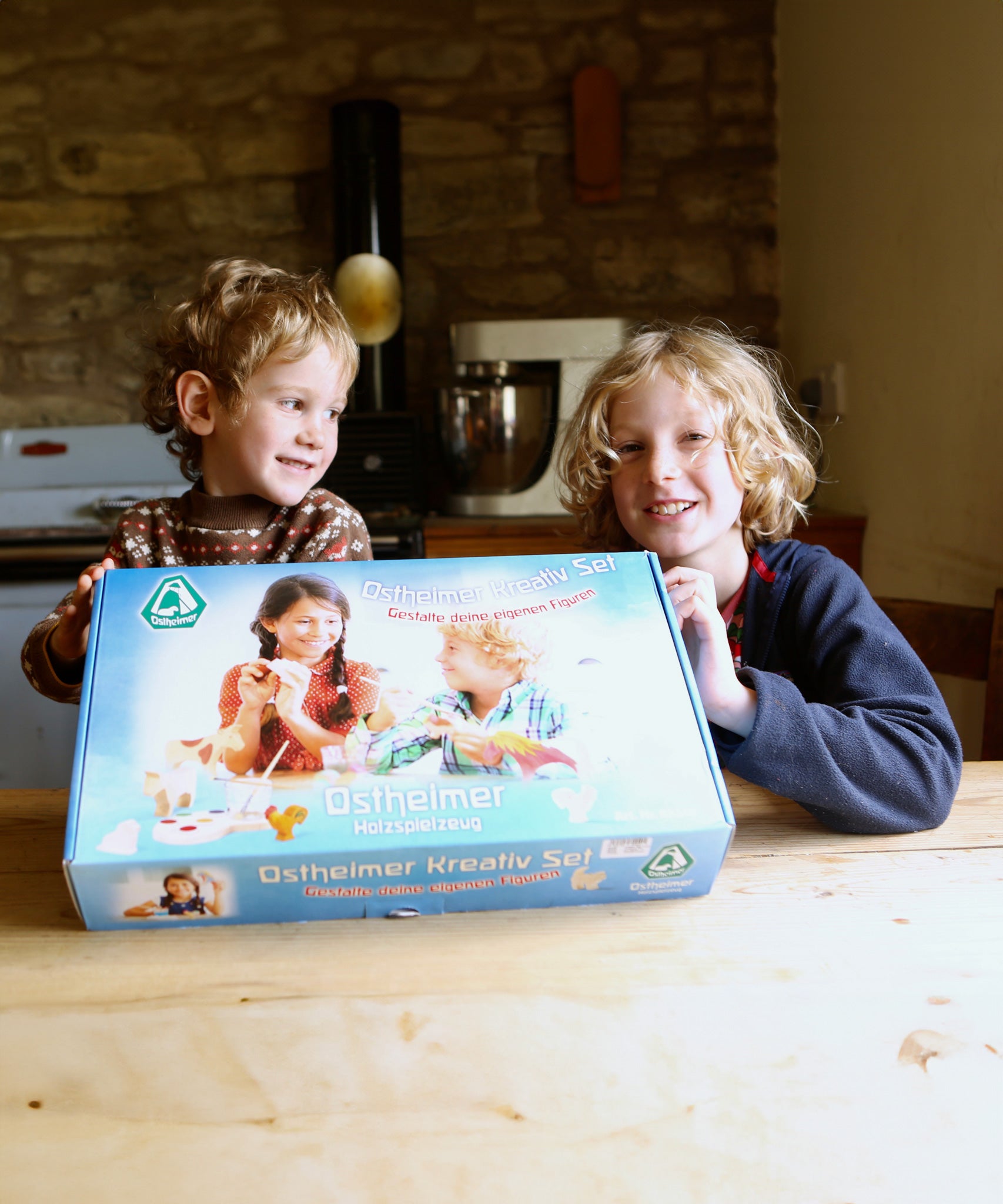 Two children smiling and holding up the Ostheimer paint your own creative set. The set is in it's packaging. 