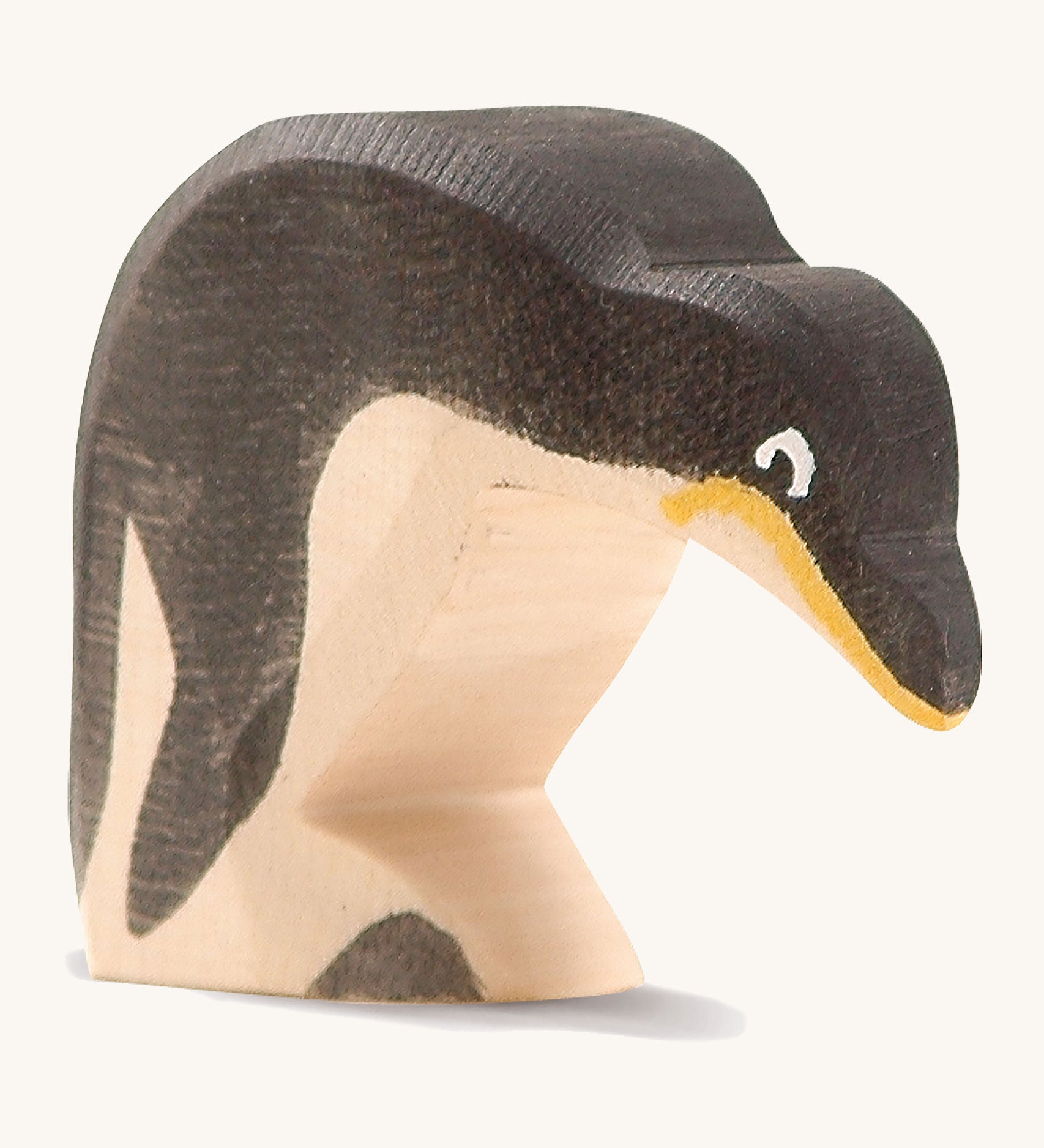 A wooden Ostheimer penguin figure with its head down on a cream background.