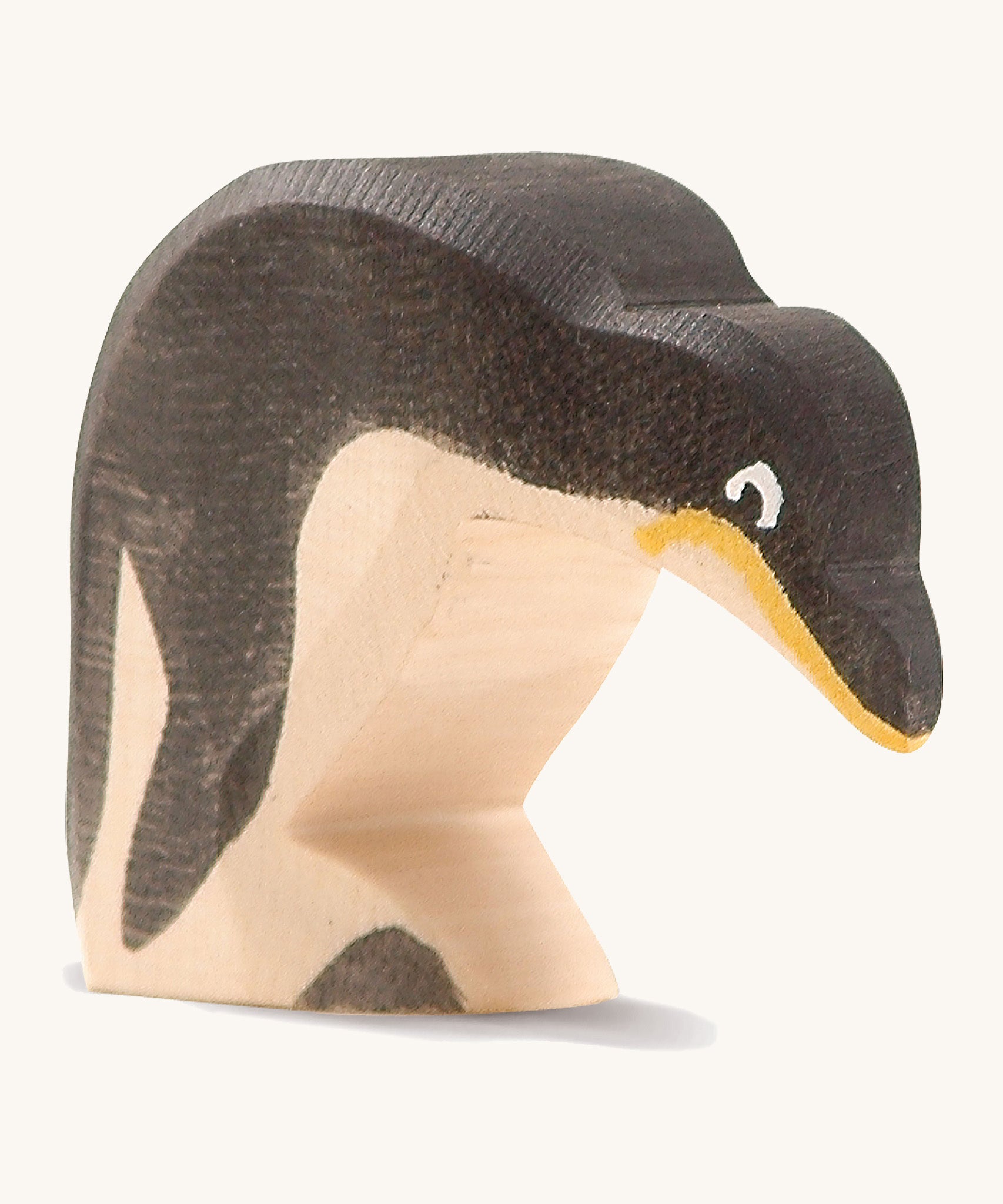 A wooden Ostheimer penguin figure with its head down on a cream background.