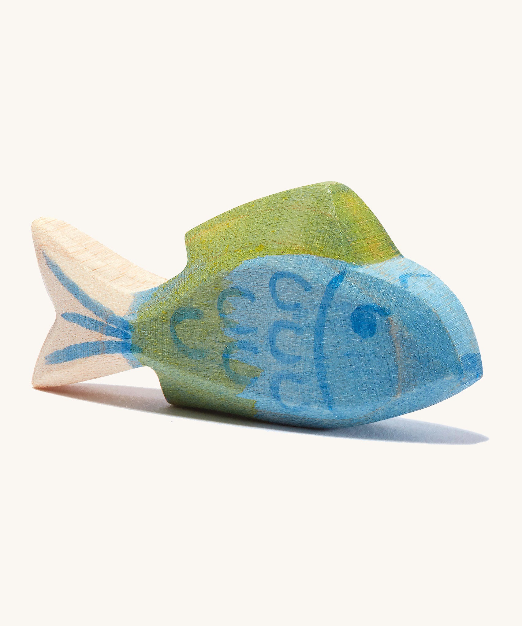 A blue wooden Ostheimer fish figure with green fins in a cream background.