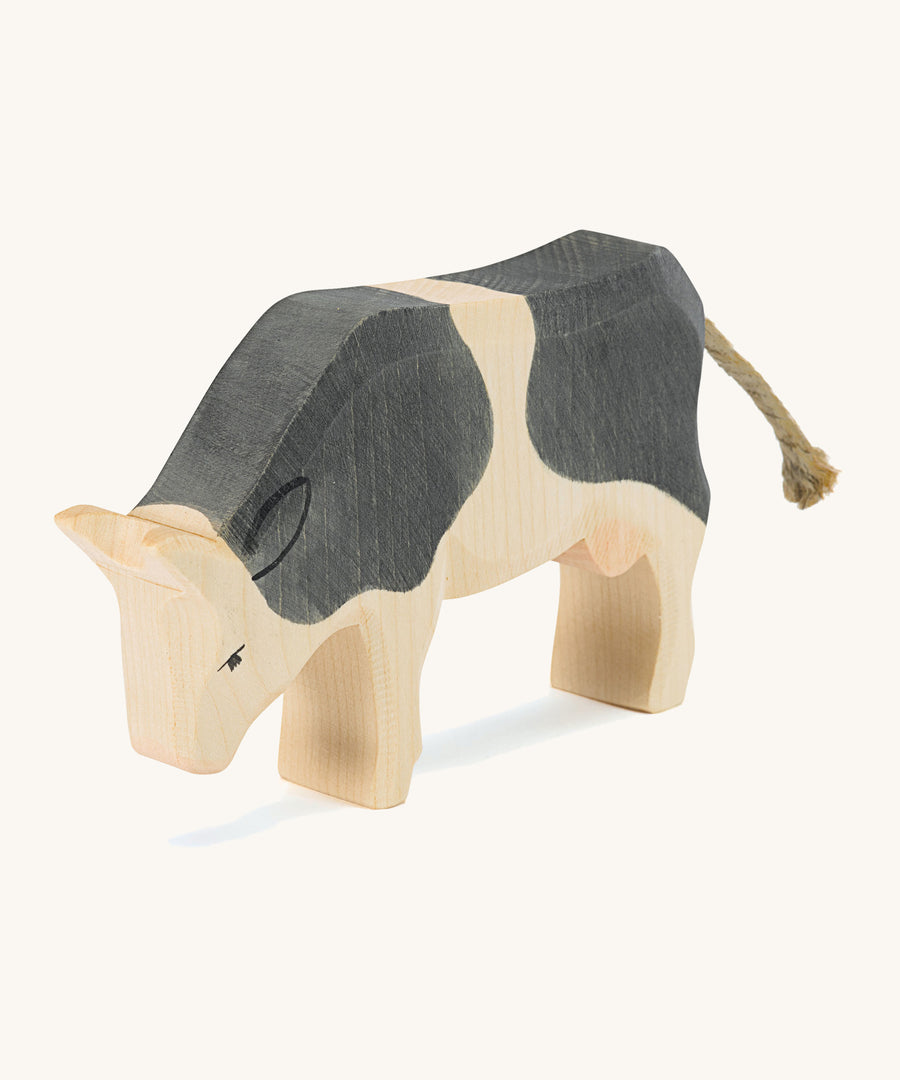 A wooden black and white Ostheimer standing cow figure on a cream background.