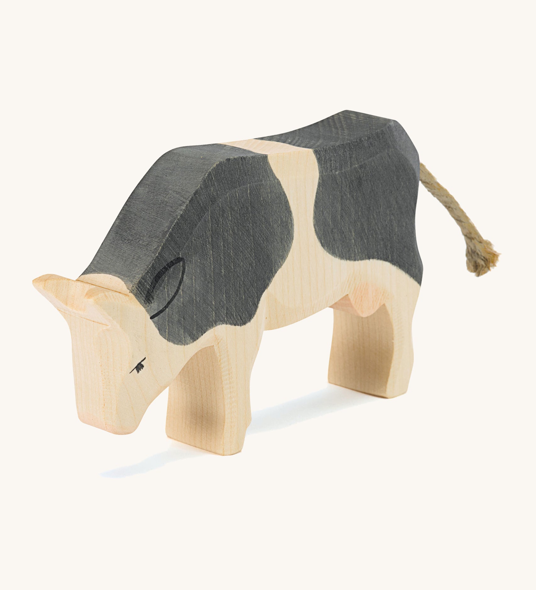 A wooden black and white Ostheimer standing cow figure on a cream background.