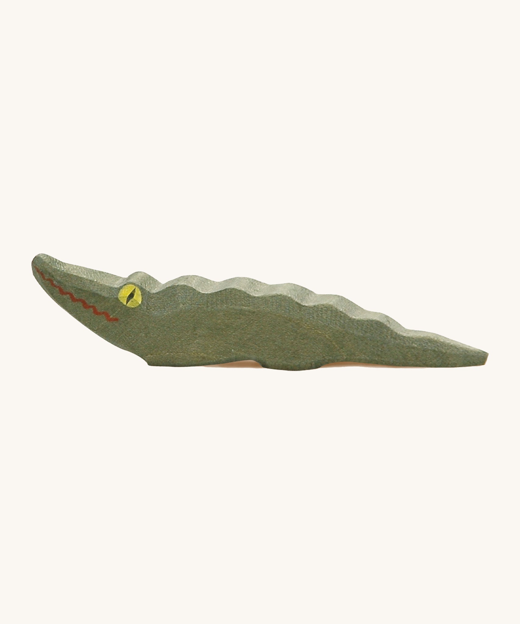 A wooden Ostheimer crocodile figure with yellow eyes on a cream background.