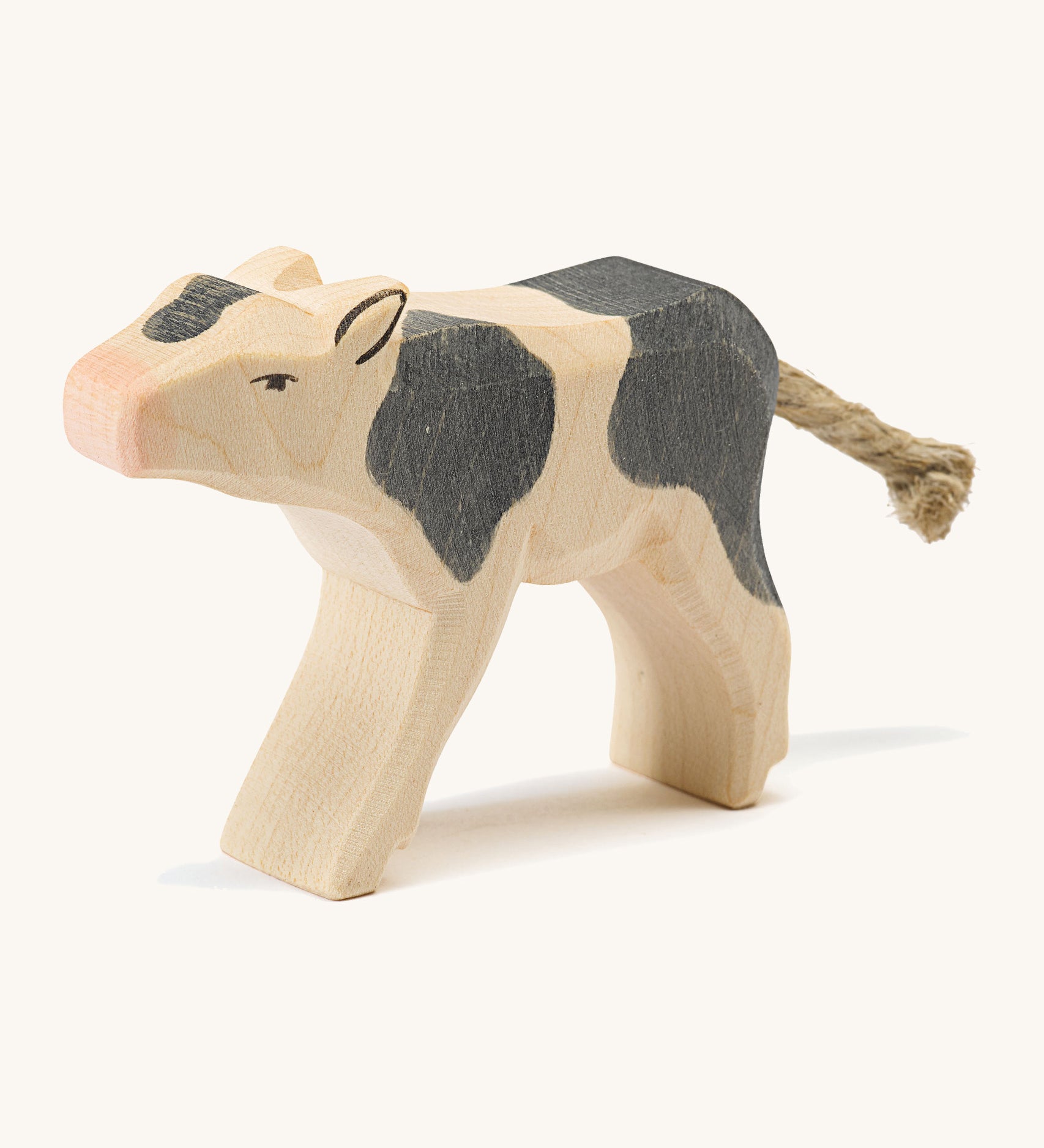 A wooden black and white Ostheimer drinking calf figure on a cream background.