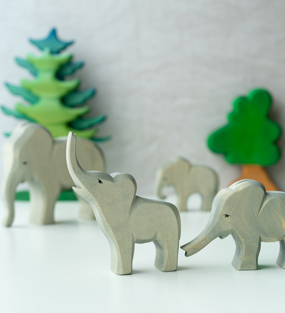 2 Ostheimer wooden elephant toy figures stood on a white table in front of some wooden Bumbu tree toys