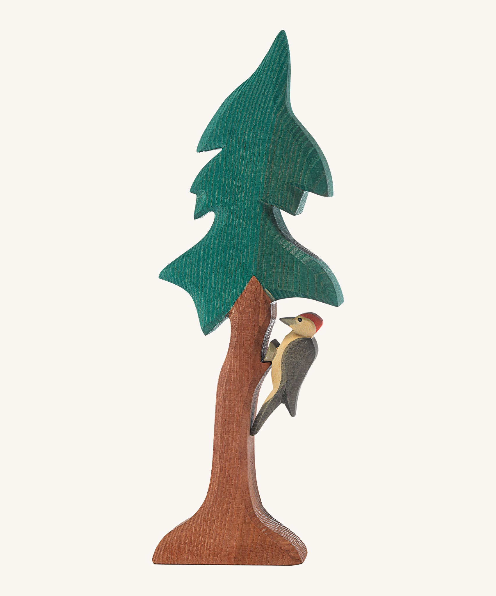 A wooden Ostheimer fir tree with a wooden Ostheimer woodpecker perched on the tree trunk on a cream background.