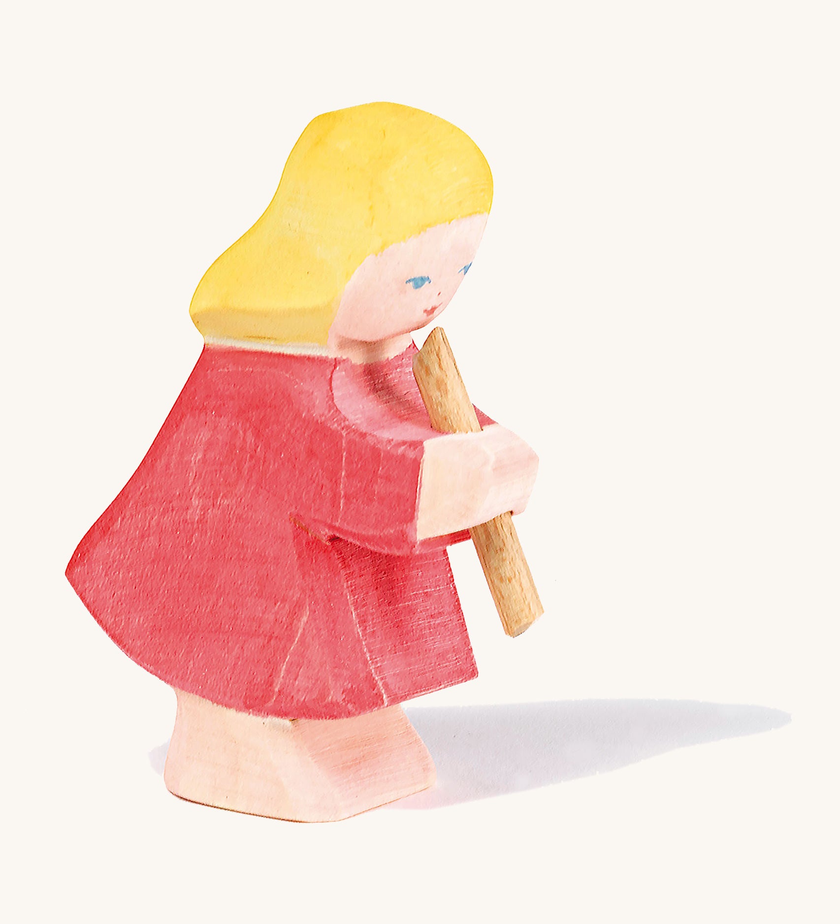 A Ostheimer wooden girl figure wearing a red dress playing a flute on a cream background.