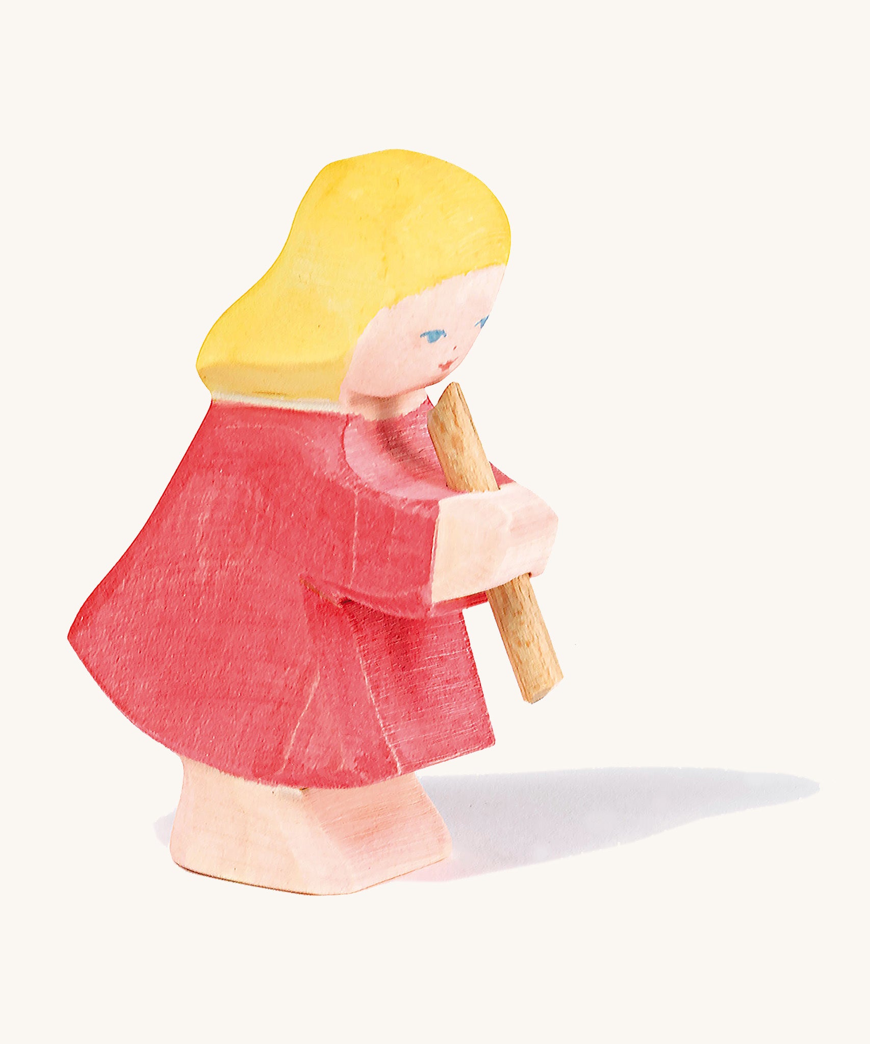 A Ostheimer wooden girl figure wearing a red dress playing a flute on a cream background.