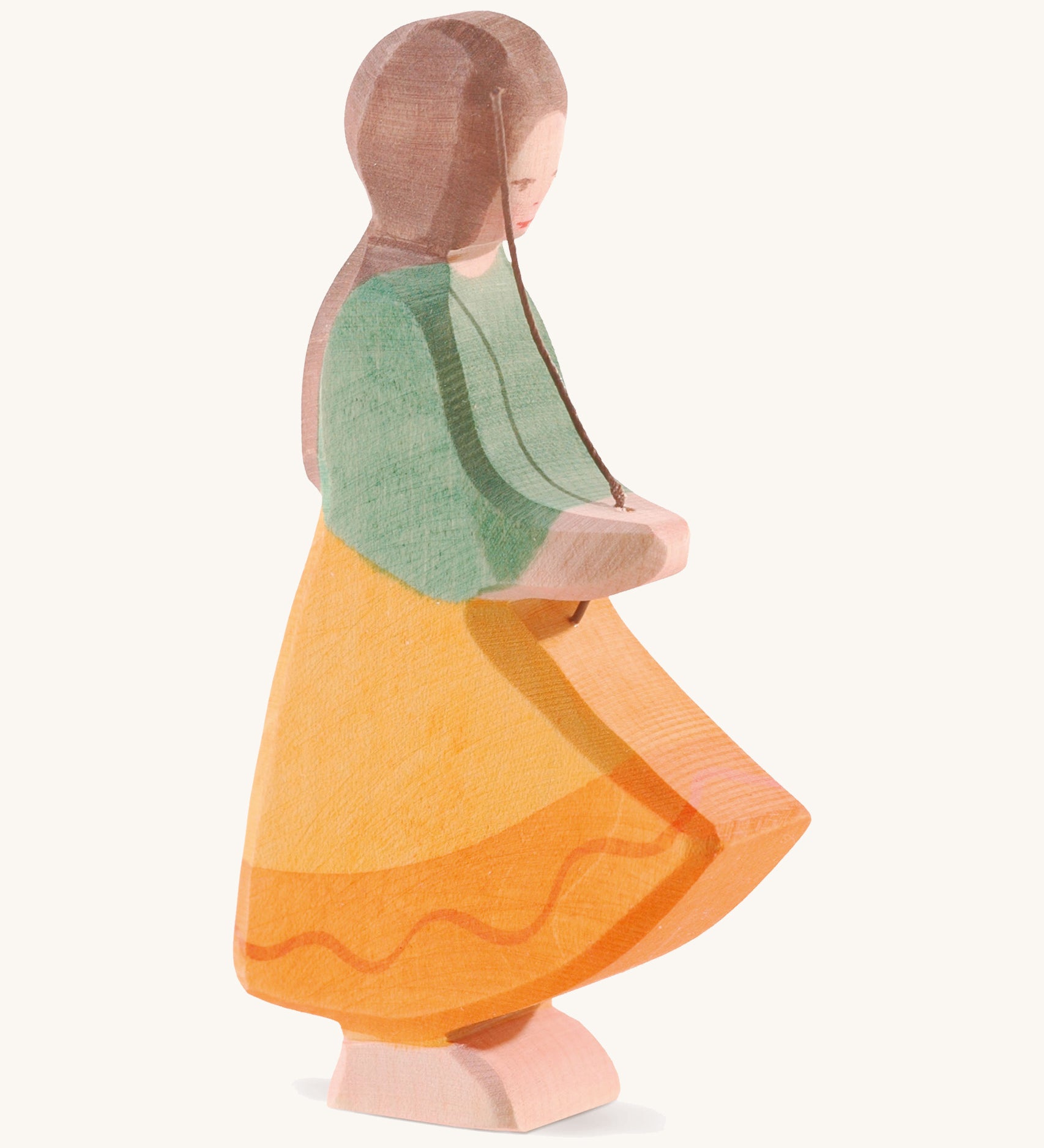 A wooden Ostheimer goose girl figure wearing a orange dress and green top with brown hair on a cream background.