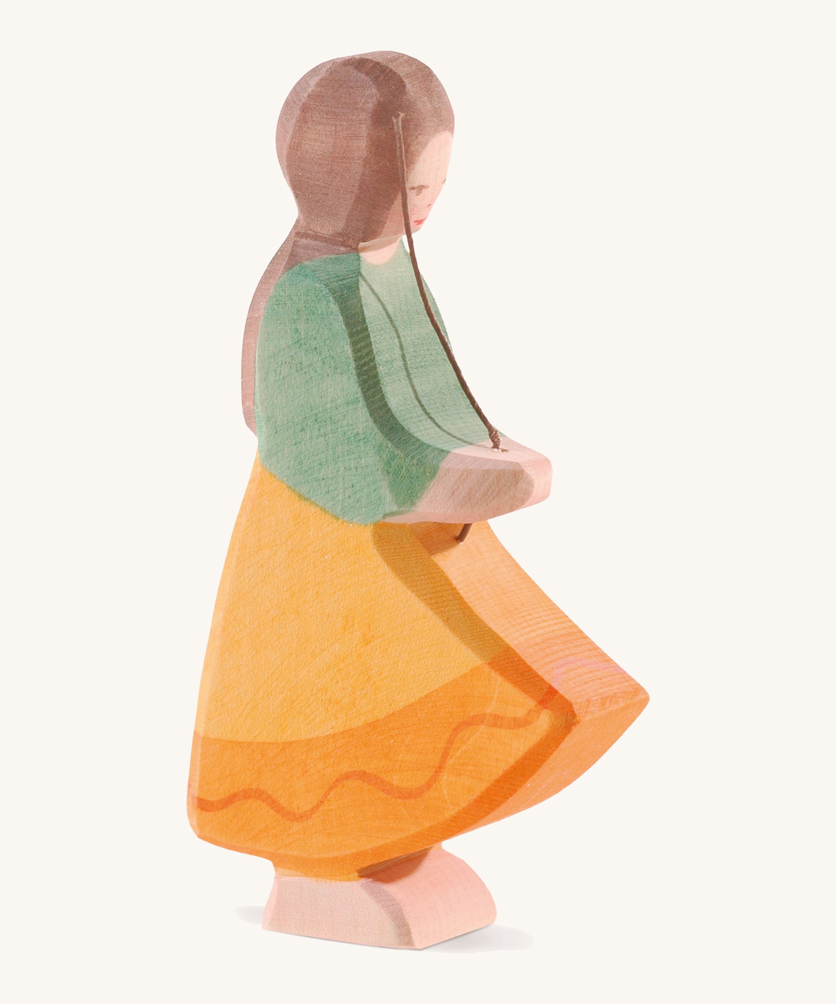 A wooden Ostheimer goose girl figure wearing a orange dress and green top with brown hair on a cream background.