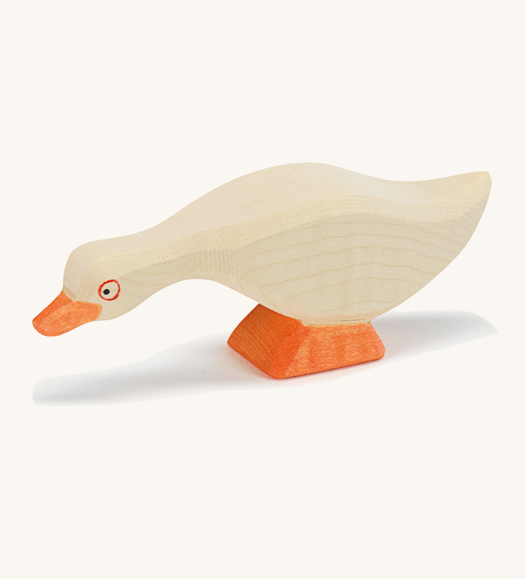 A white wooden Ostheimer goose figure with its head low on a cream background.