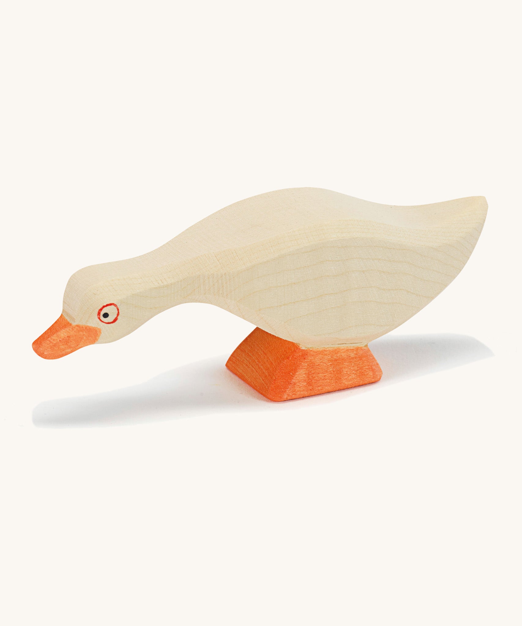 A white wooden Ostheimer goose figure with its head low on a cream background.