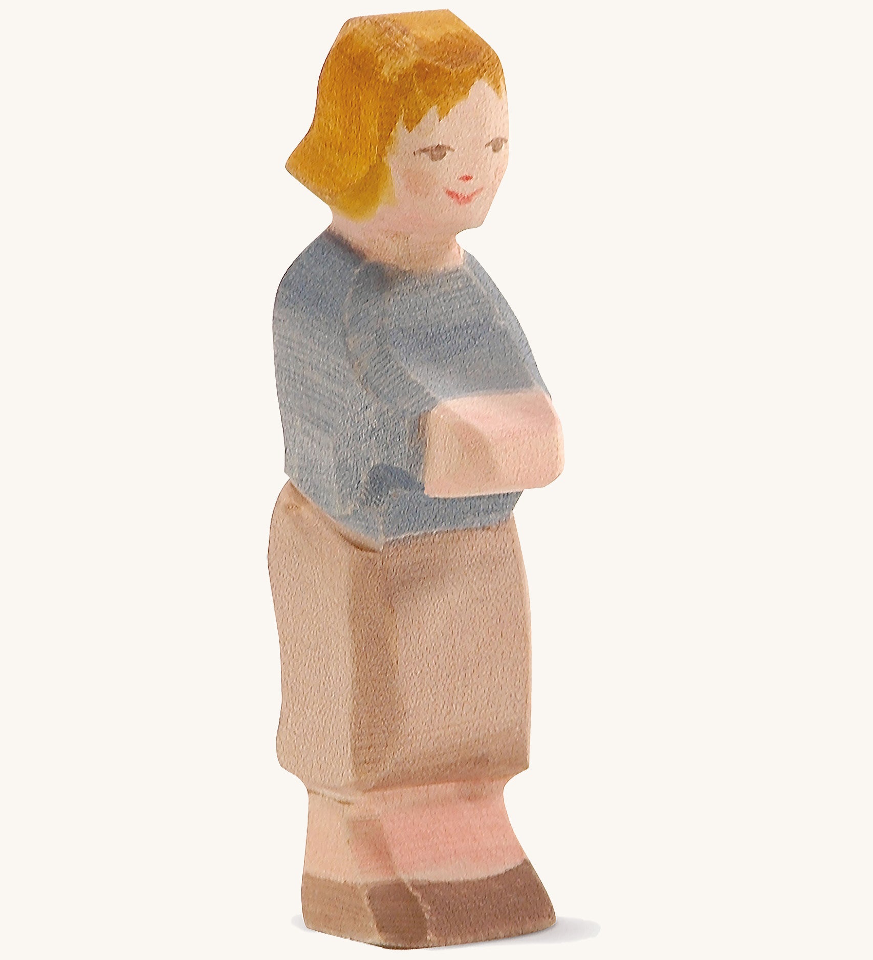 A wooden Ostheiner Hansel figure with brown hair wearing a blue jumper and brown trousers on a cream background.