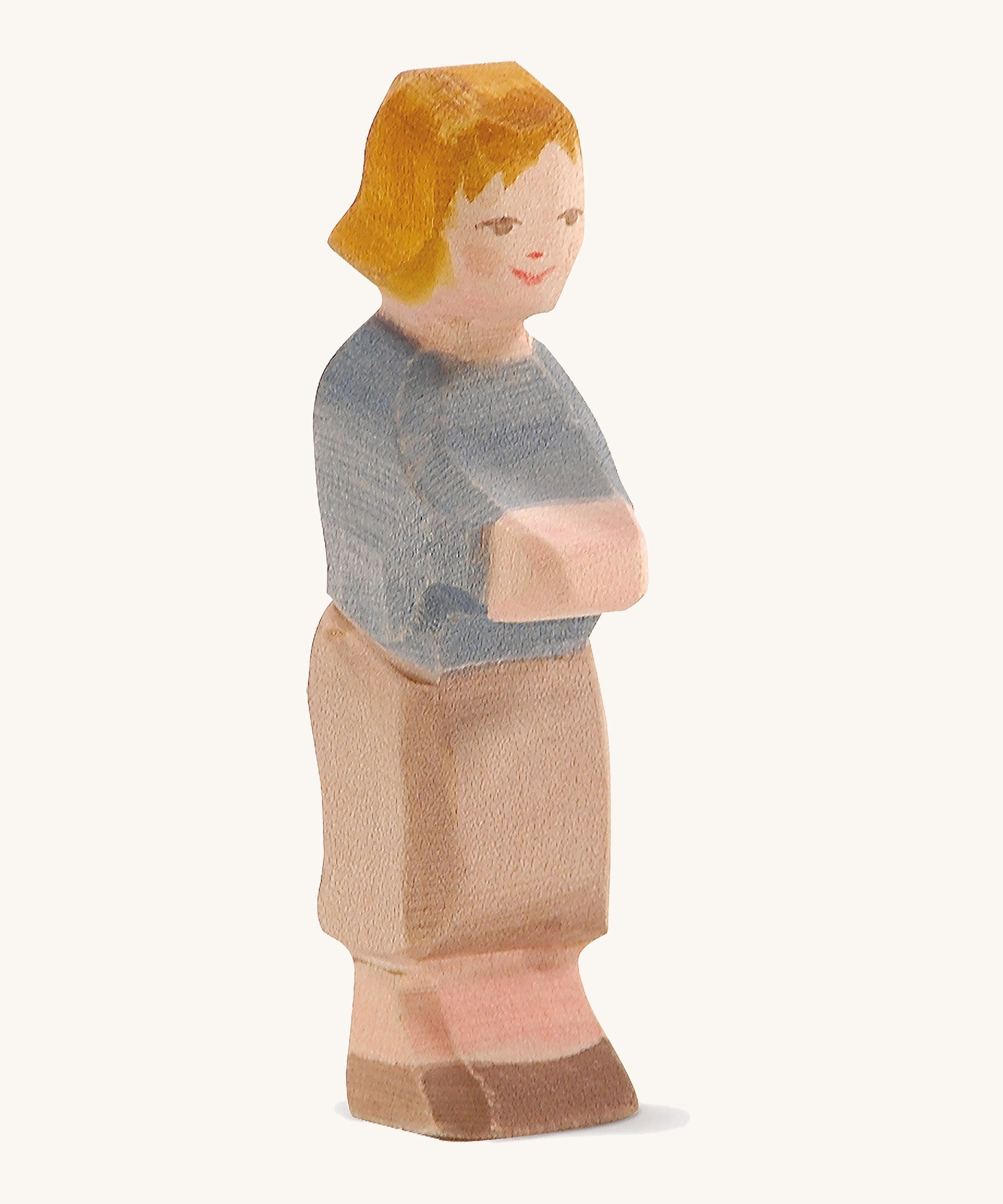 A wooden Ostheiner Hansel figure with brown hair wearing a blue jumper and brown trousers on a cream background.