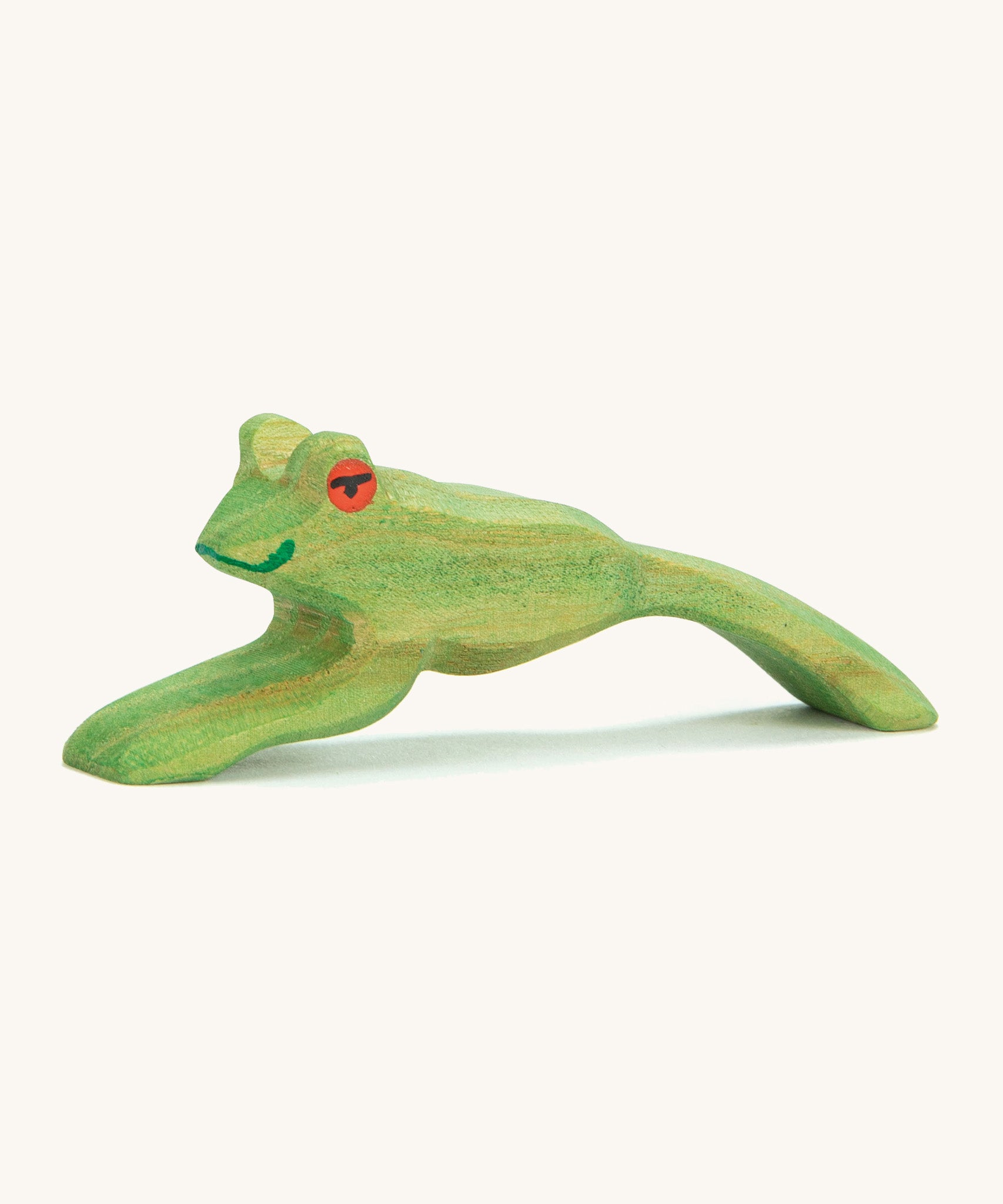 A green wooden Ostheimer jumping frog figure on a cream background.