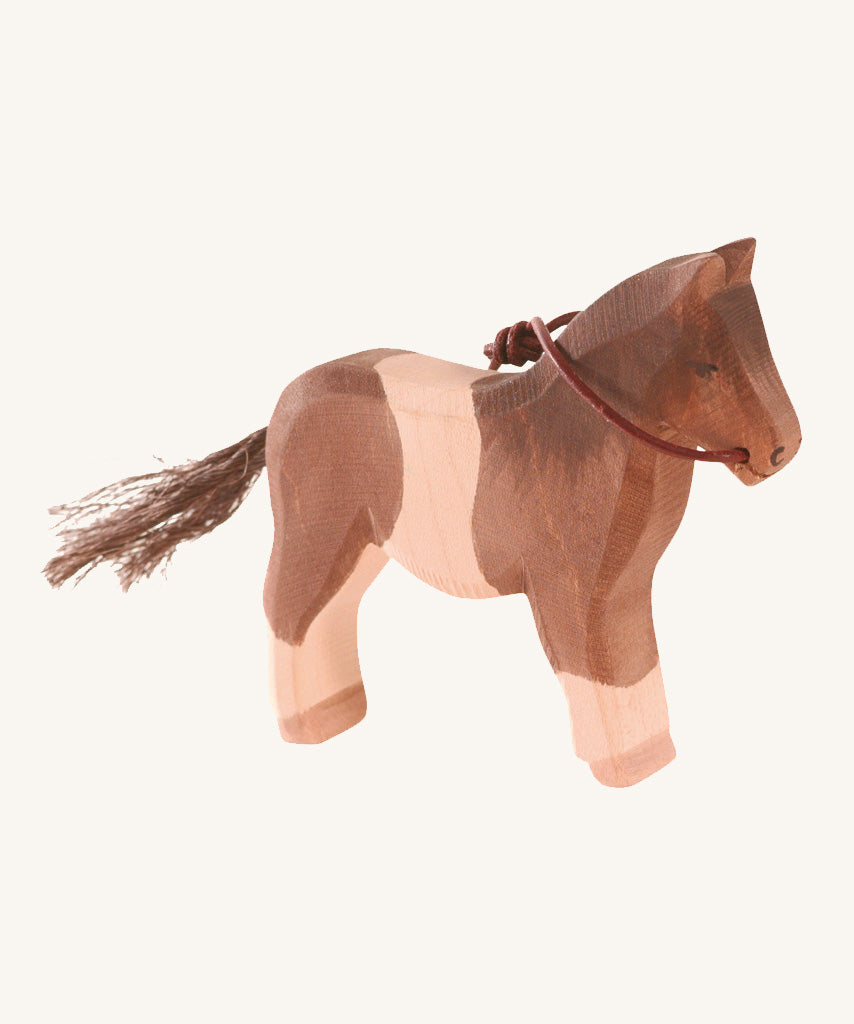 A white and brown wooden Ostheimer pony figure on a cream background.