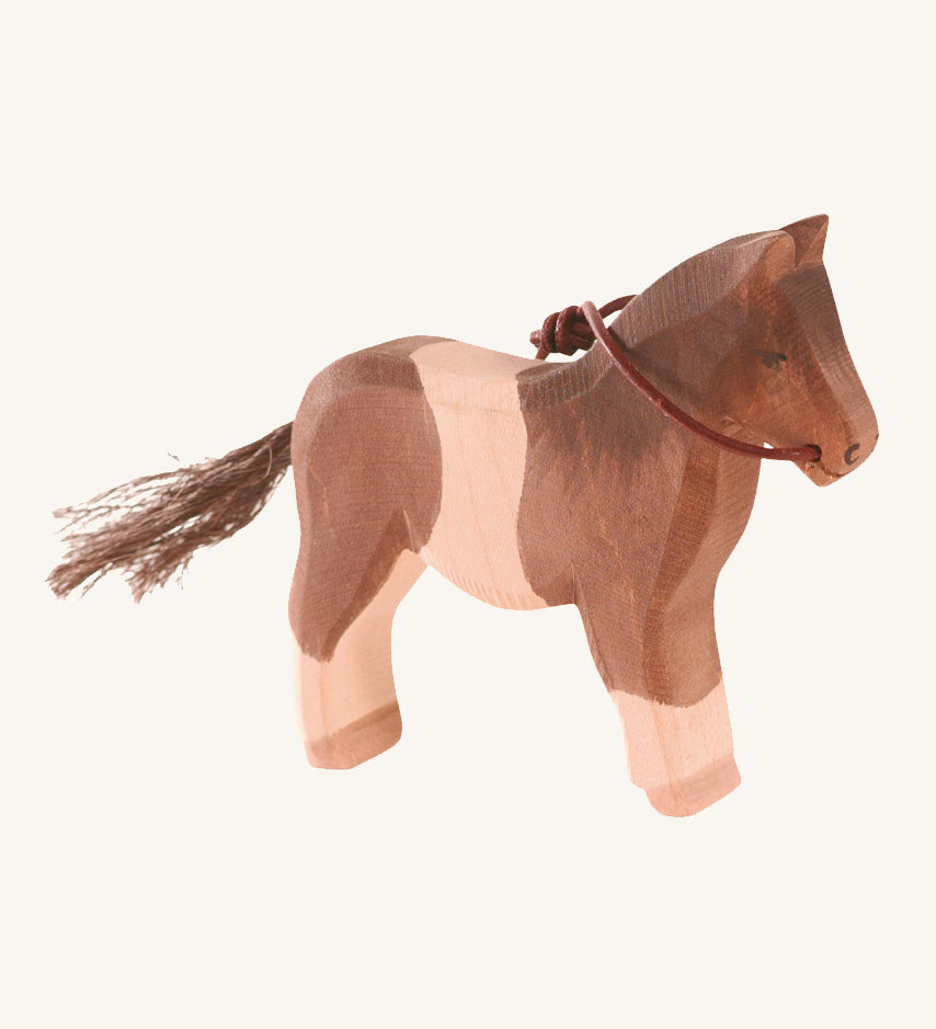 A white and brown wooden Ostheimer pony figure on a cream background.