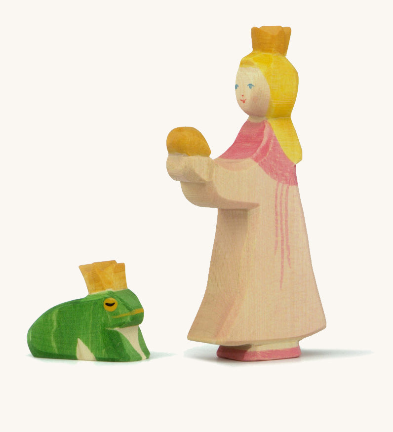 A wooden Ostheimer princess figure wearing a pink dress standing next to a king frog figure on a cream background.