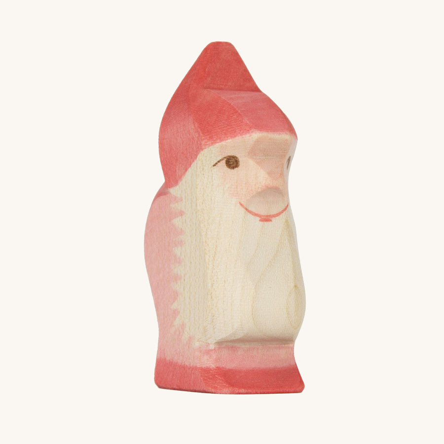 Ostheimer Wooden Red Dwarf toy. A handmade and crafted wooden dwarf figure with a red hat and shoes, and a light red outfit and natural wood coloured beard. The Red Dwarf shows the smooth natural wood grain of the figure and is sat on a cream background