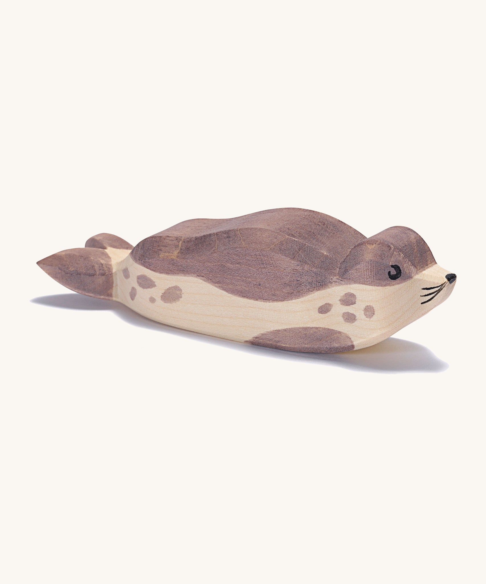 A wooden resting Ostheimer sea lion figure on a cream background.