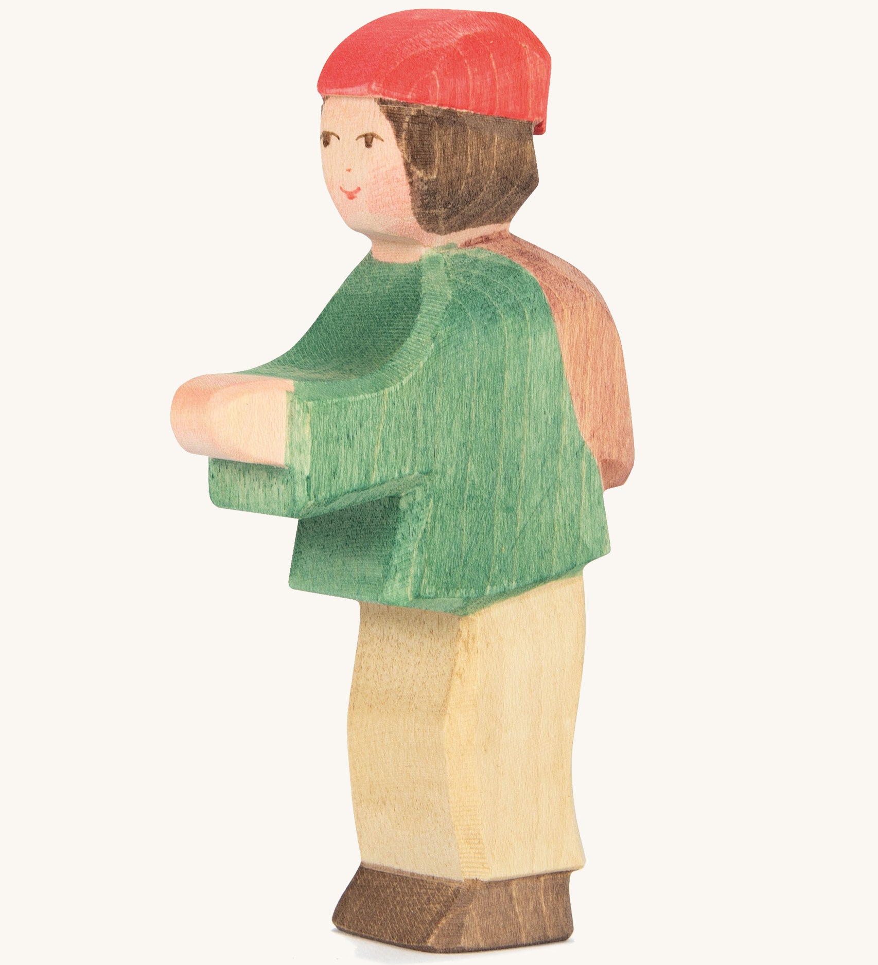 A wooden Ostheimer shepherd boy figure weaing a green coat, brown trousers and a red hat on a cream background.