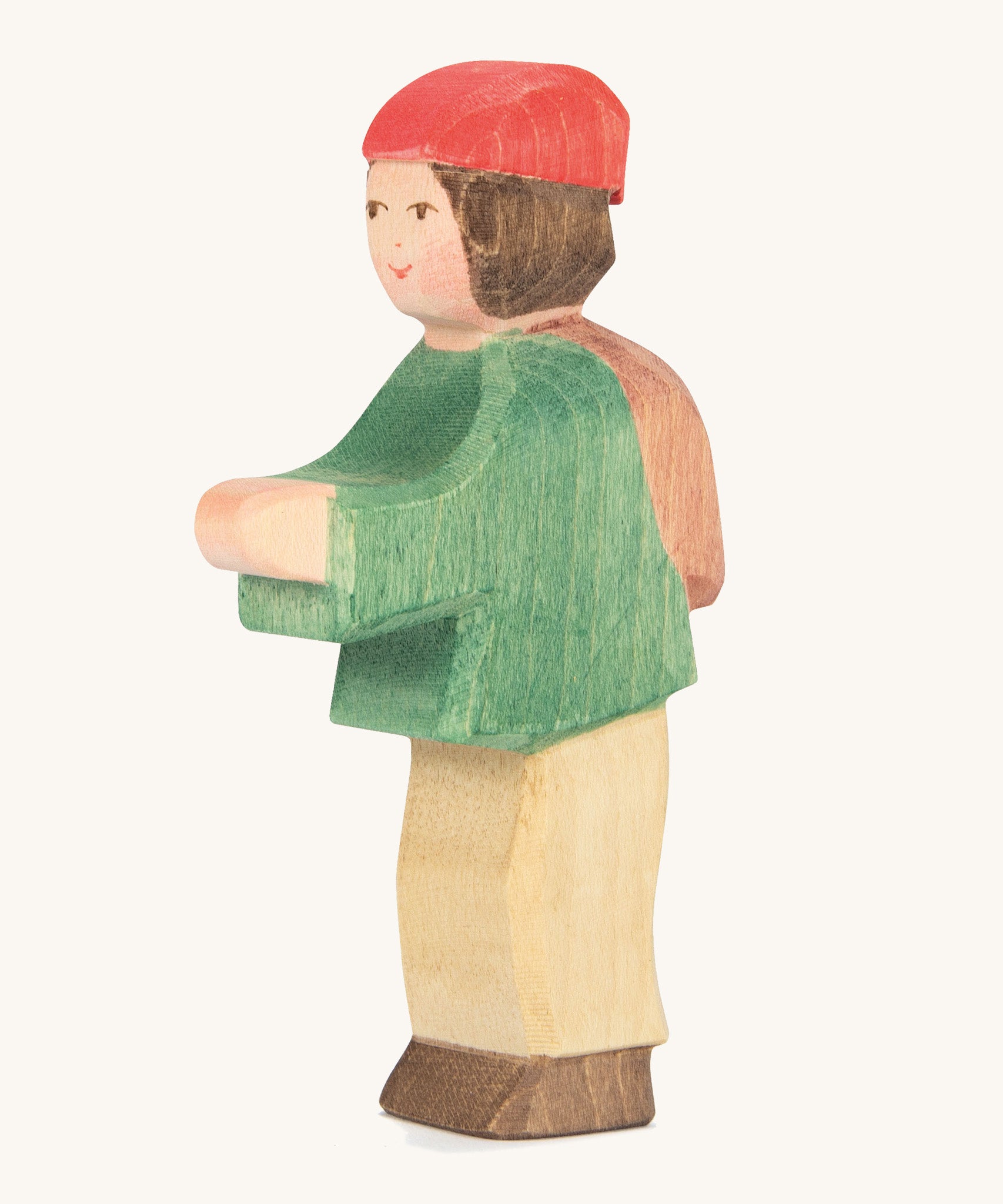 A wooden Ostheimer shepherd boy figure weaing a green coat, brown trousers and a red hat on a cream background.