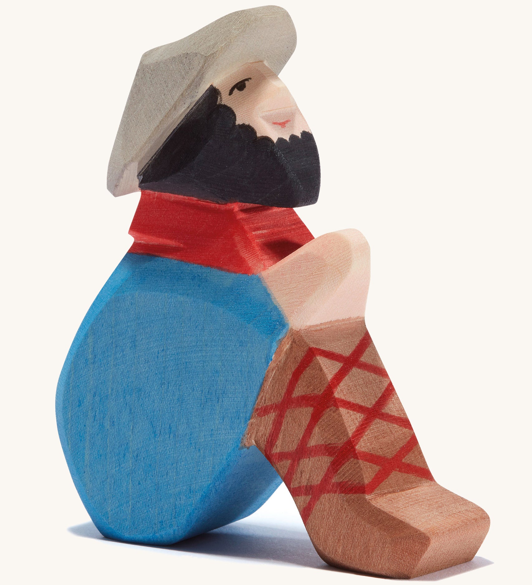 A wooden sitting Ostheimer shepherd figure wearing a blue coat, brown trousers and a grey hat on a cream background.