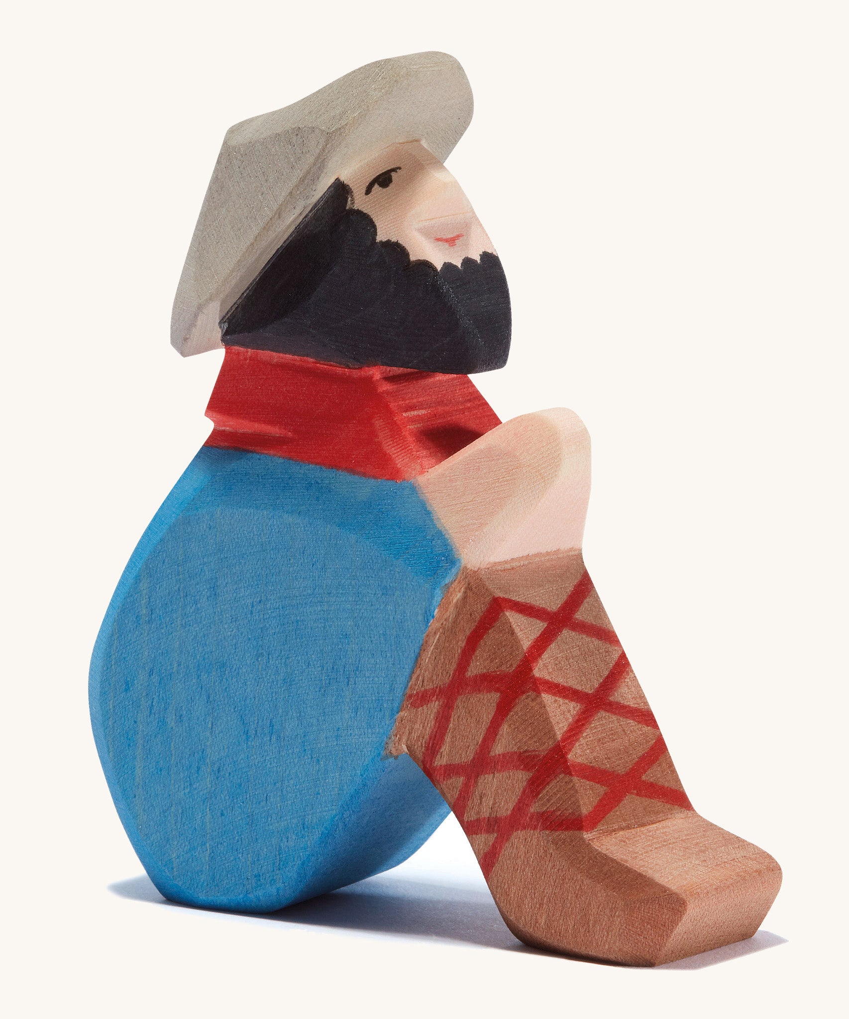 A wooden sitting Ostheimer shepherd figure wearing a blue coat, brown trousers and a grey hat on a cream background.