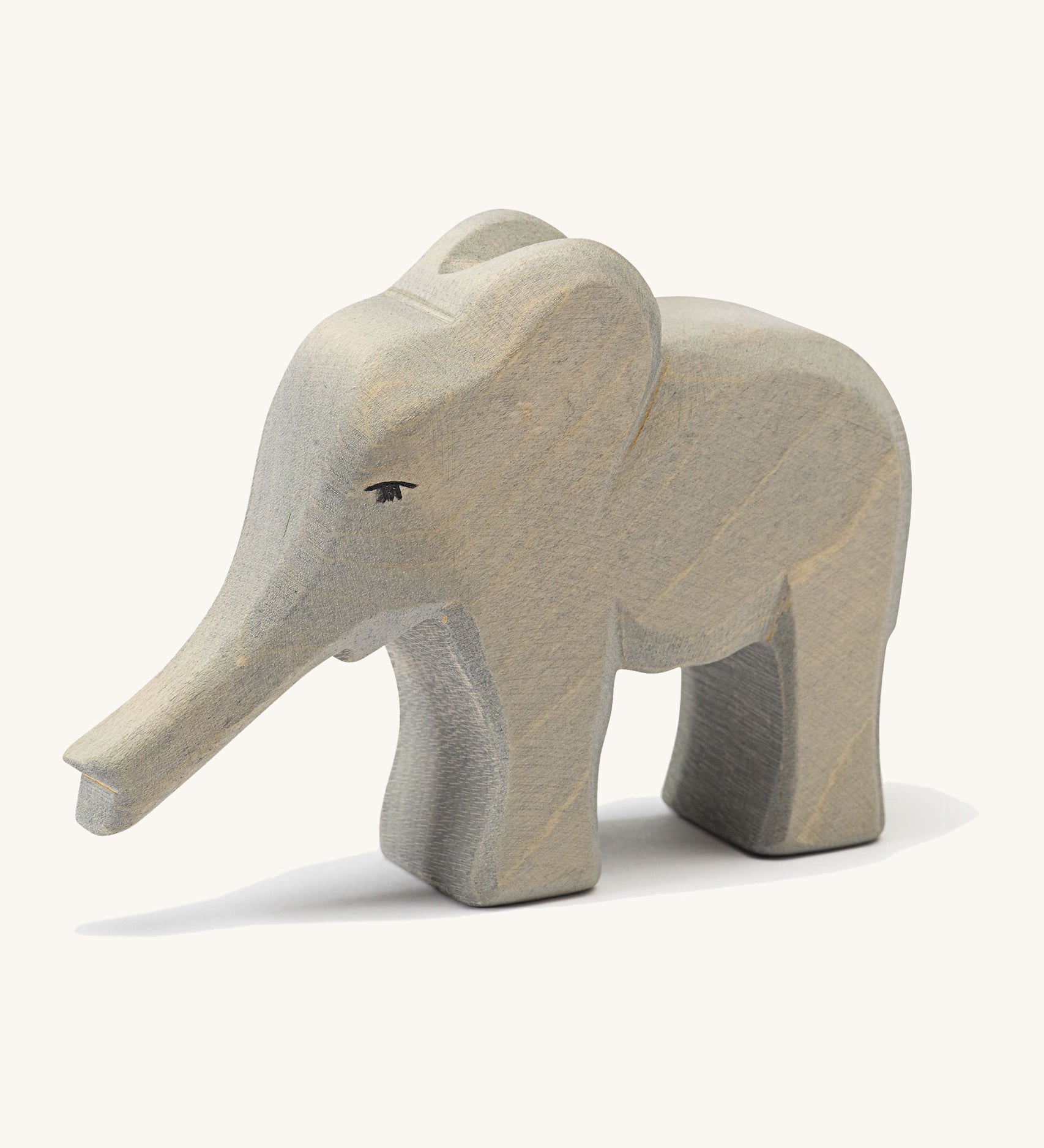 A small wooden Ostheimer elephant figure with its trunk out on a cream background.