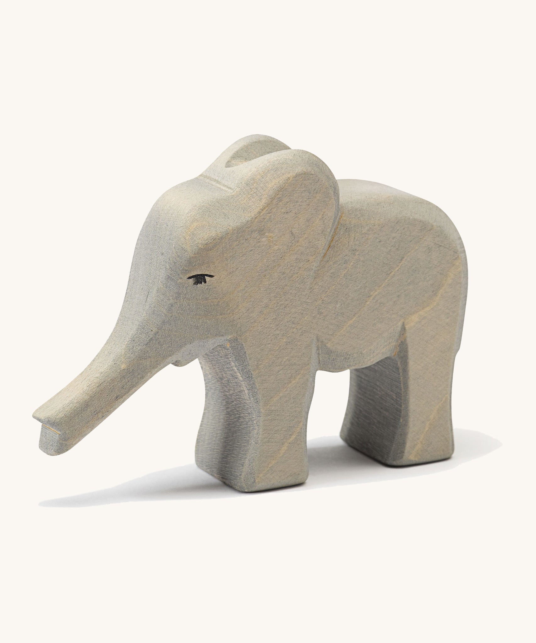 A small wooden Ostheimer elephant figure with its trunk out on a cream background.